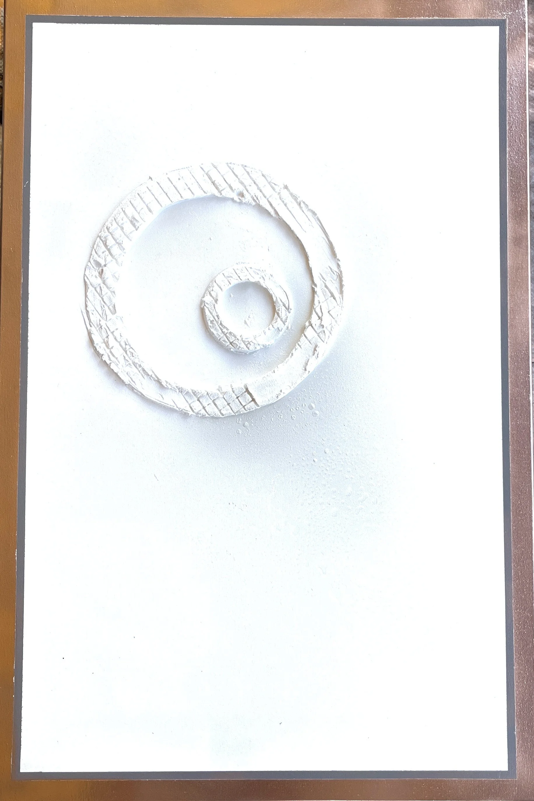 A white circular spiral pattern made from textured material, placed on a white background. The spiral starts from the center and expands outward.
