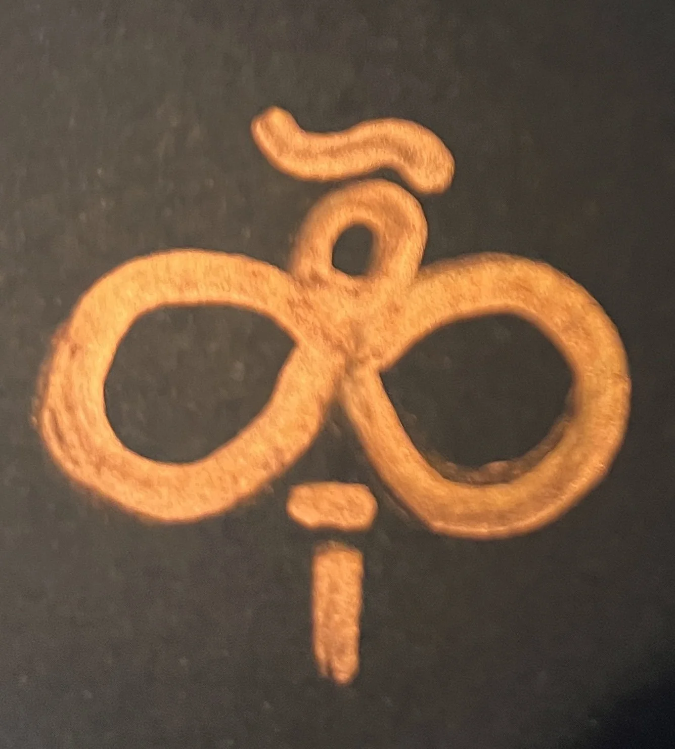 Close-up of a copper or bronze ornament with a decorative swirl design on a black background.