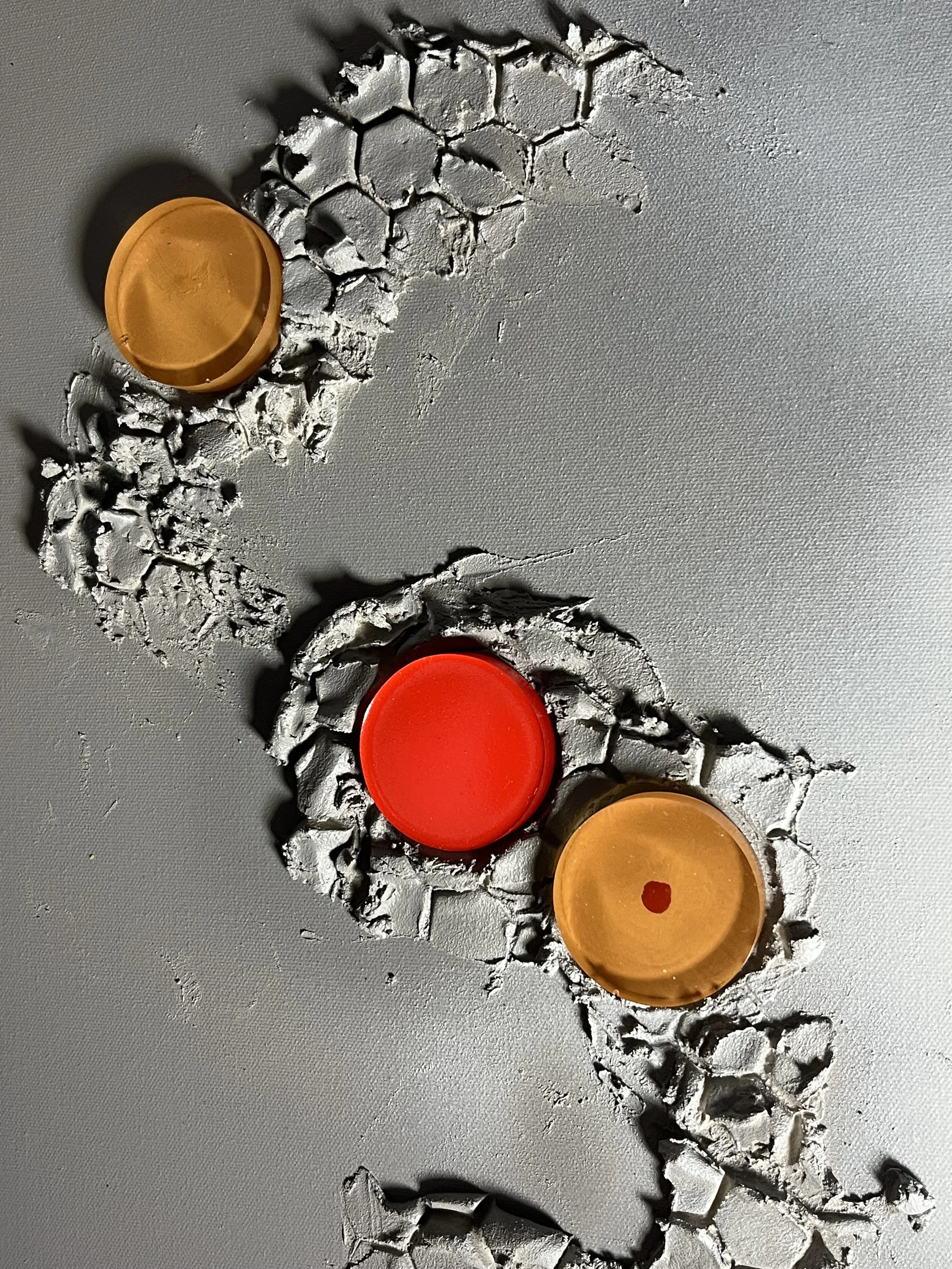 Close-up of metallic surface with honeycomb pattern and three scattered small round objects in orange, red, and yellow.