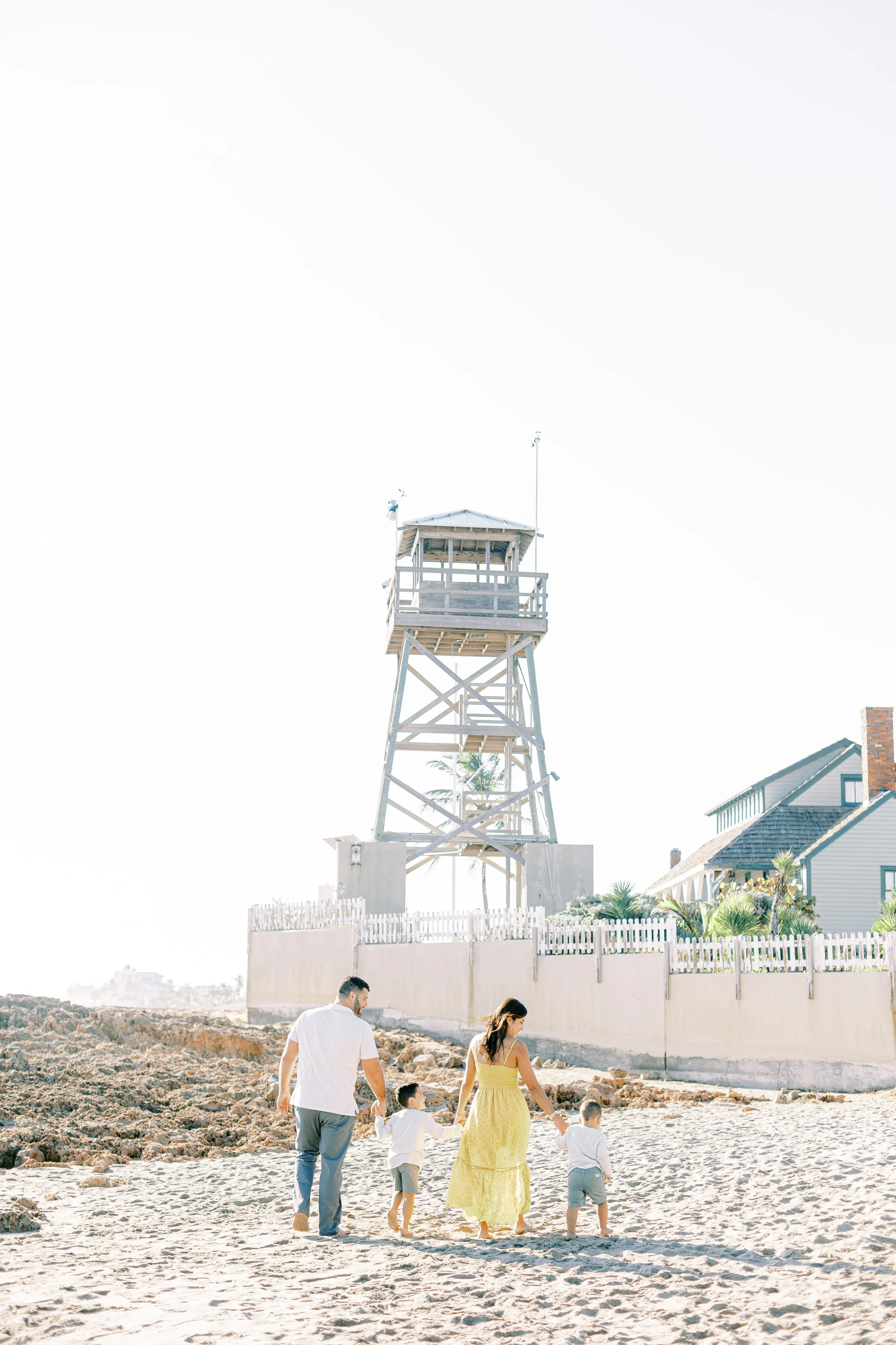 Family walking on beach at the House of Refuge in Stuart Florida near a lighthouse with a small house and white fencing in the background.