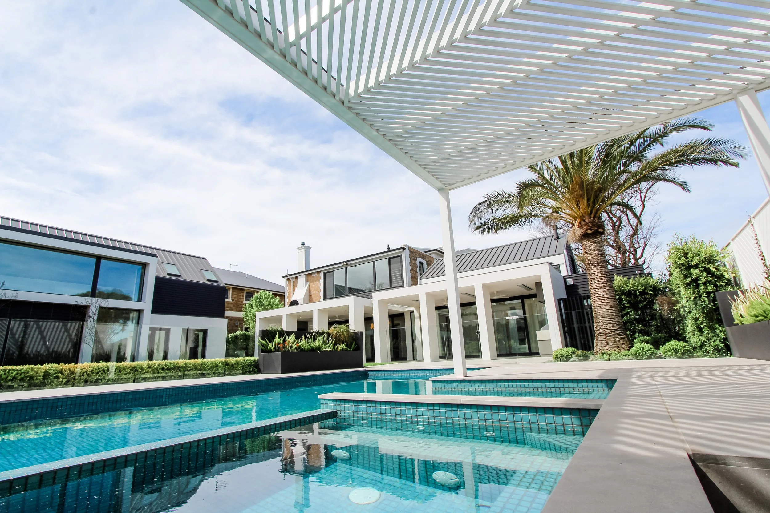 Modern house with large windows, swimming pool in the backyard, palm tree, and outdoor seating area under a white lattice pergola.