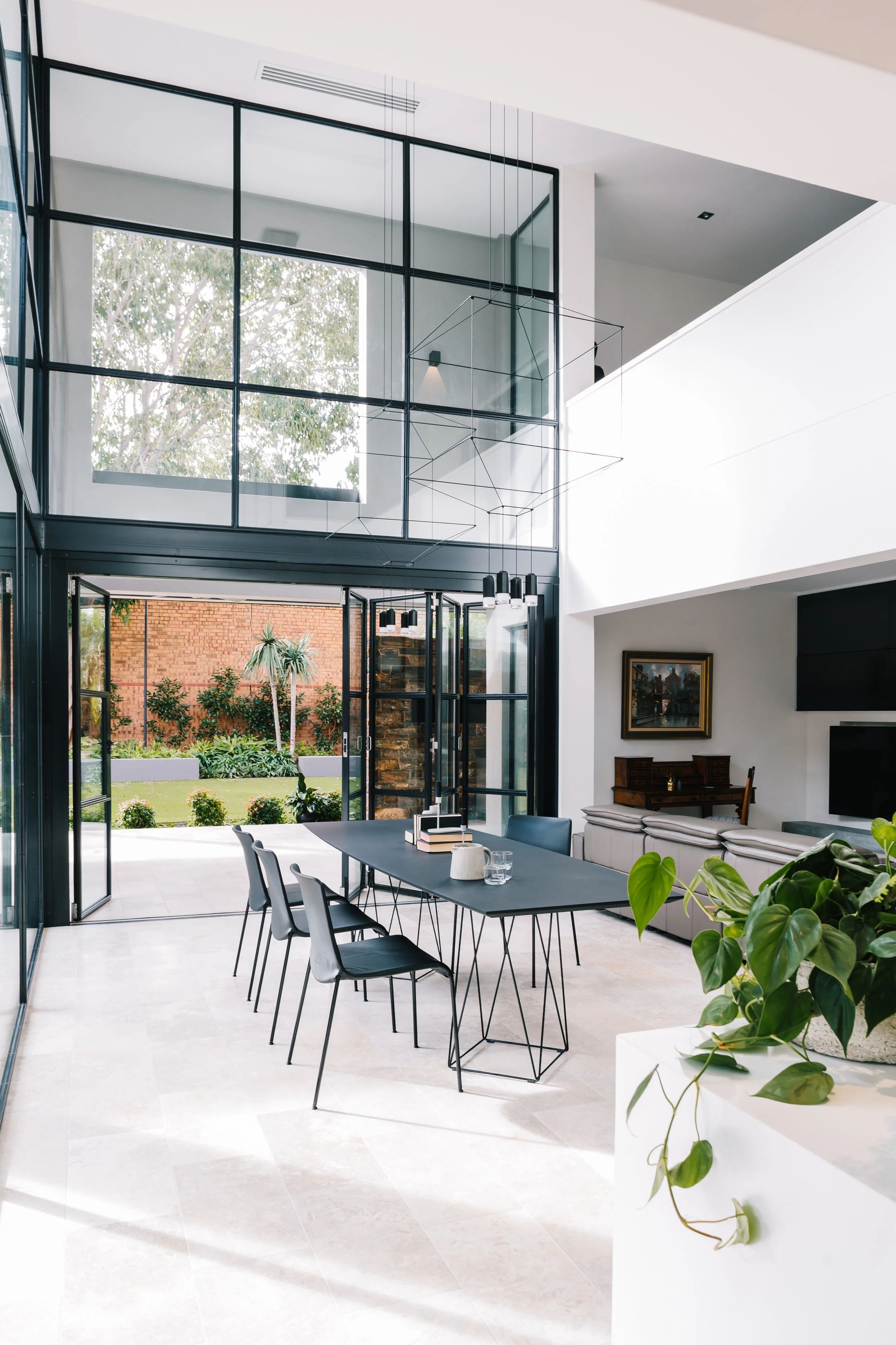Modern home interior with large glass windows and doors opening to a backyard, black dining table with chairs, and contemporary decor.