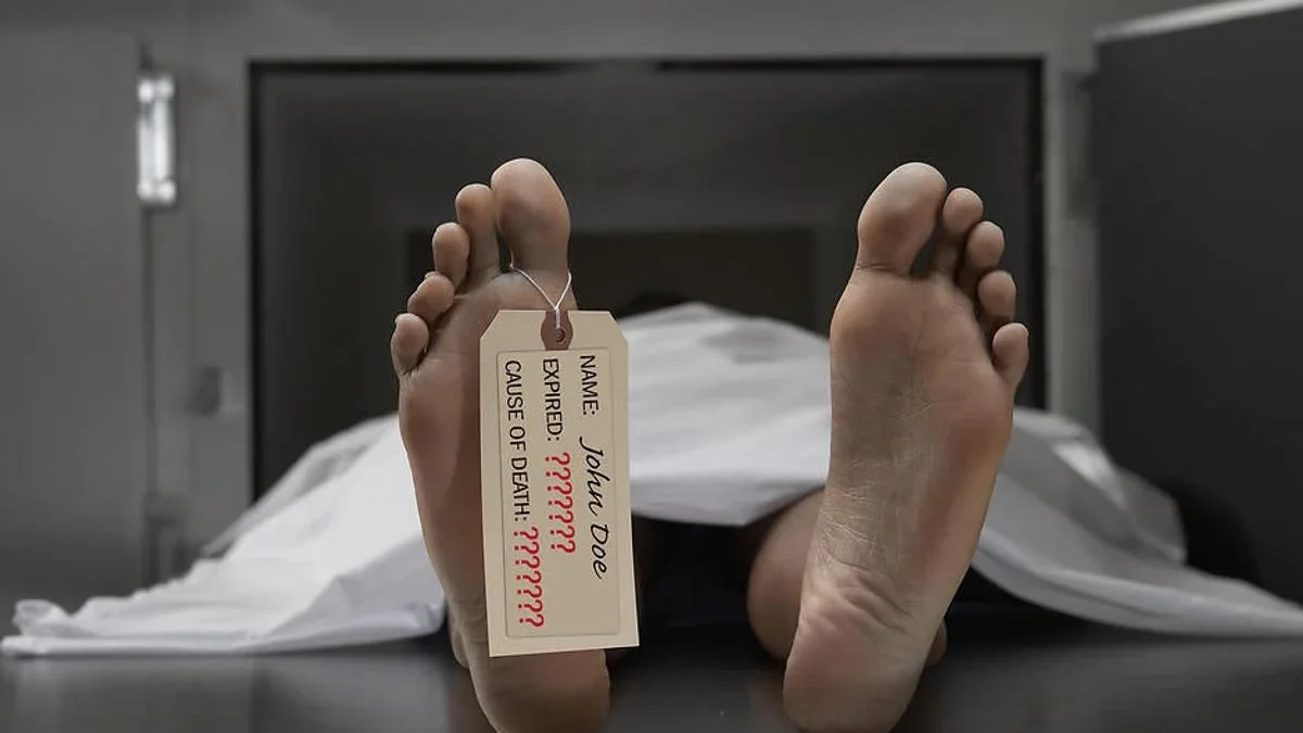 Foot of a deceased person with a funeral tag reading 'Name: John Doe, Expired: ??, Cause of Death: ??' on an open casket in a morgue.