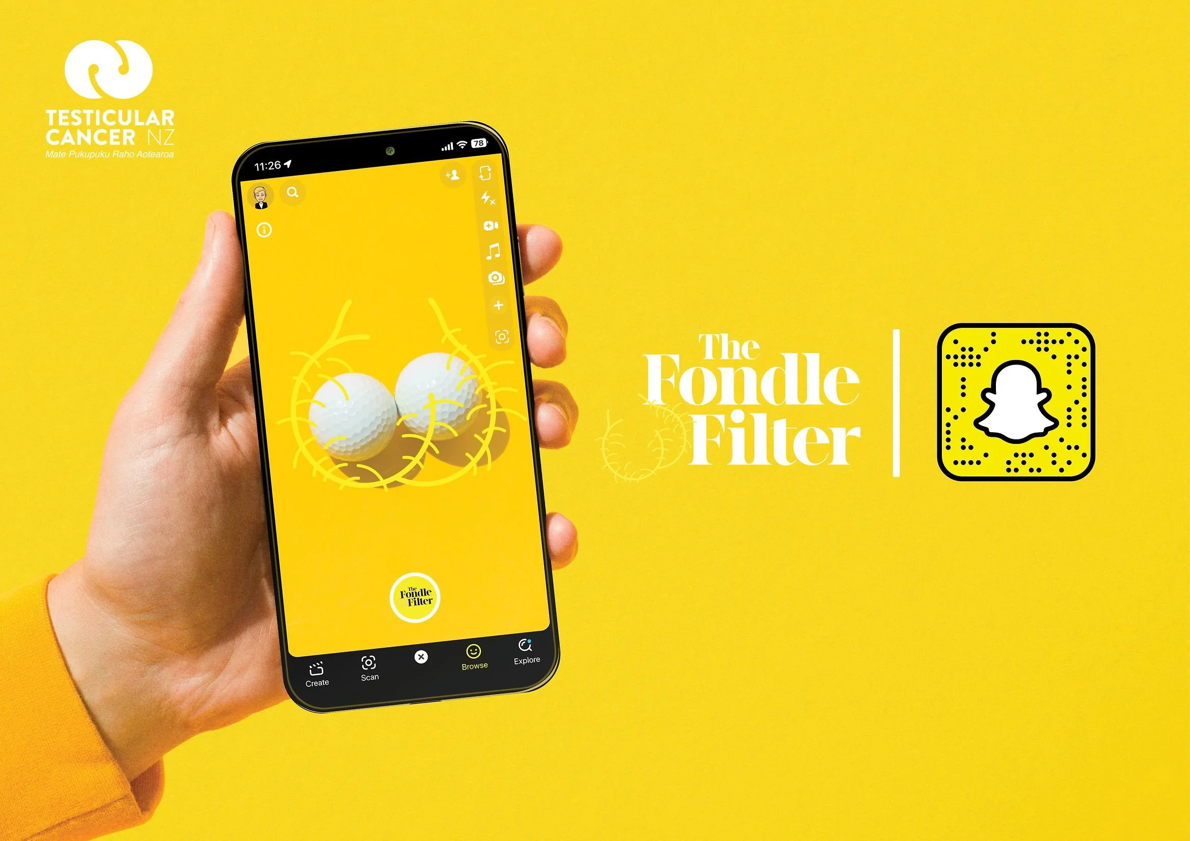 A hand holding a smartphone displaying a yellow background with two golf balls and the words "The Fundle Filler". The background of the image is yellow with the logo and text "Testicular Cancer NZ Mate Pukupuku Raho Aotearoa" in the upper left corner, and a QR code to the right of the text.