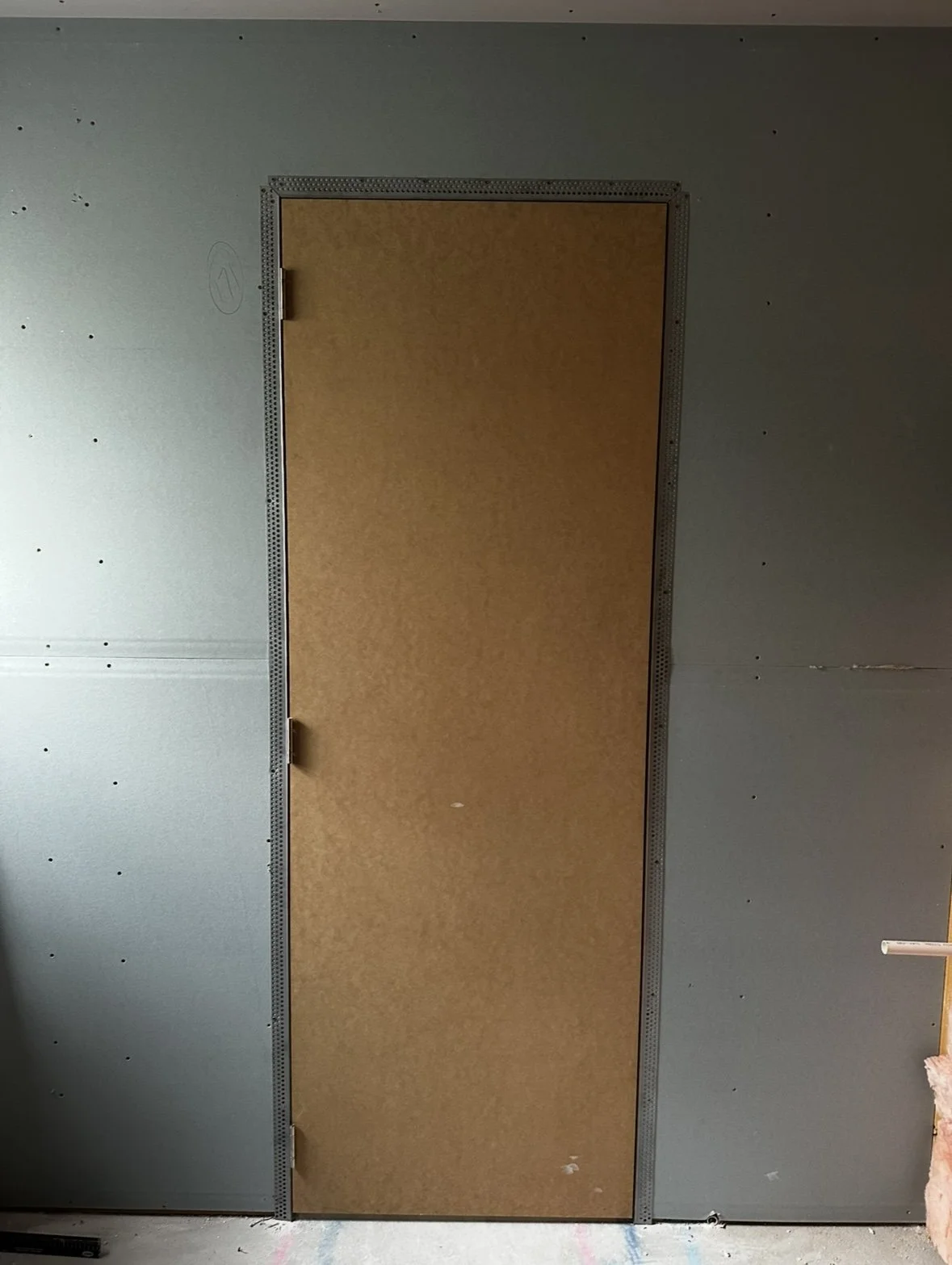 Interior of a room with gray drywall walls and a brown door in the middle.
