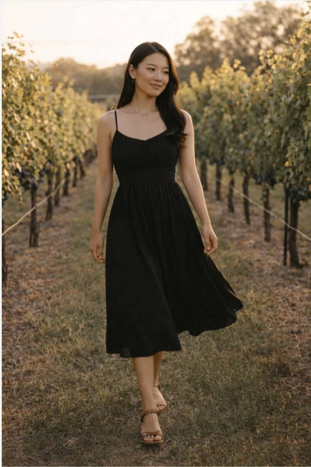 woman wearing a black midi dress walking through vineyard rows at sunset