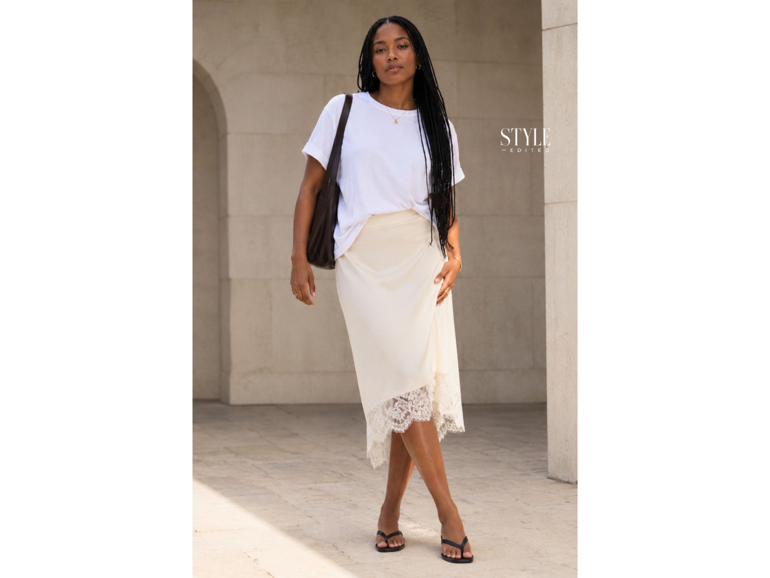 Black woman wearing a relaxed white T-shirt with a cream lace-trim midi skirt and flat leather sandals outdoors.