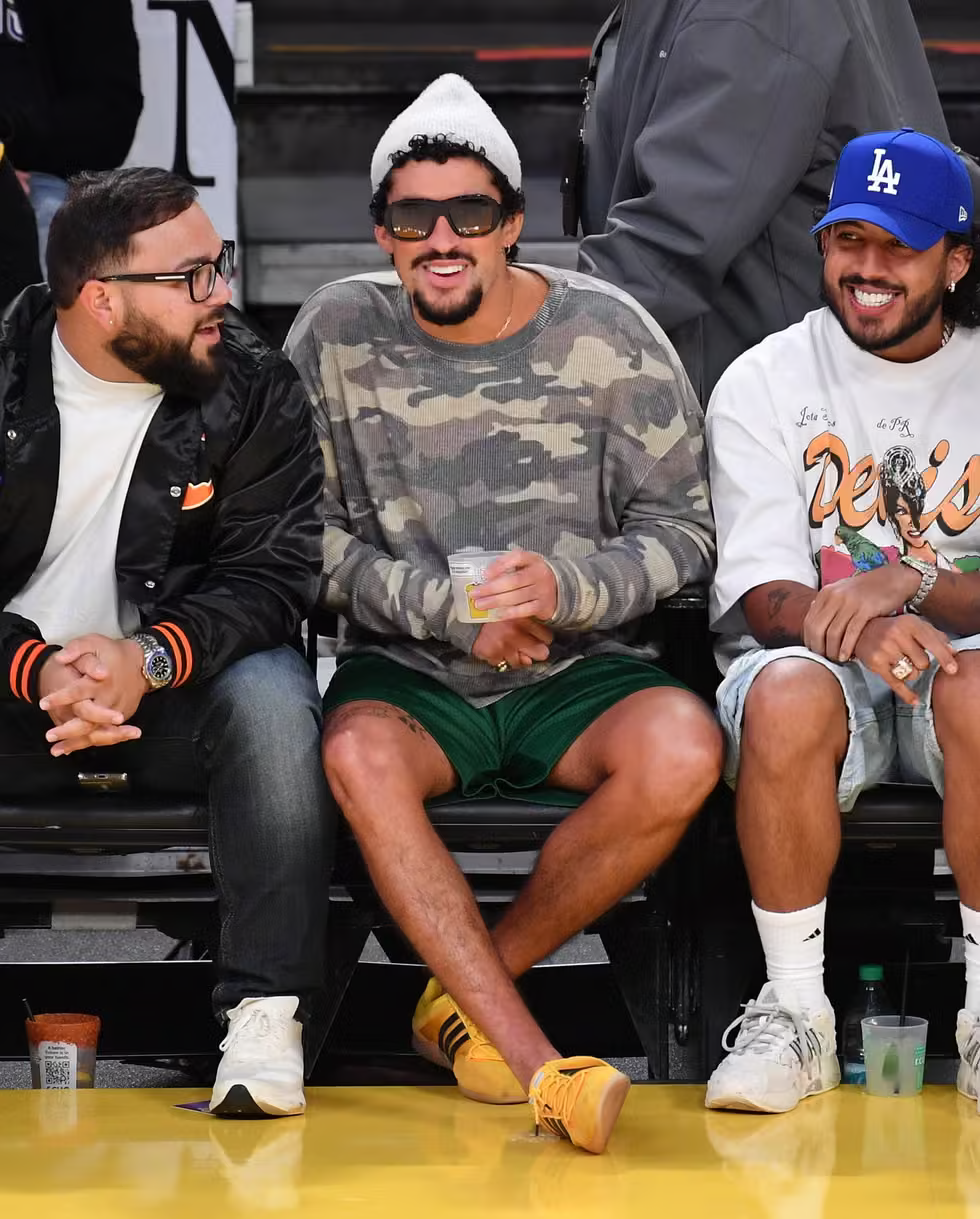 Bad Bunny wearing yellow Adidas sneakers with green shorts and camo sweater courtside