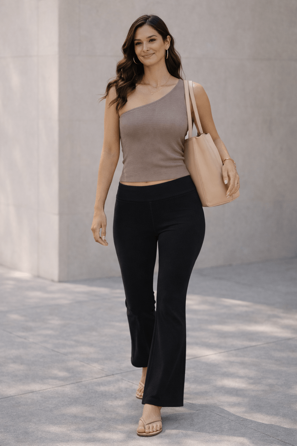 Minimal flare leggings outfit with black flare leggings, structured taupe asymmetric top, gold jewelry, tan sandals, and light neutral shoulder bag in a modern summer setting