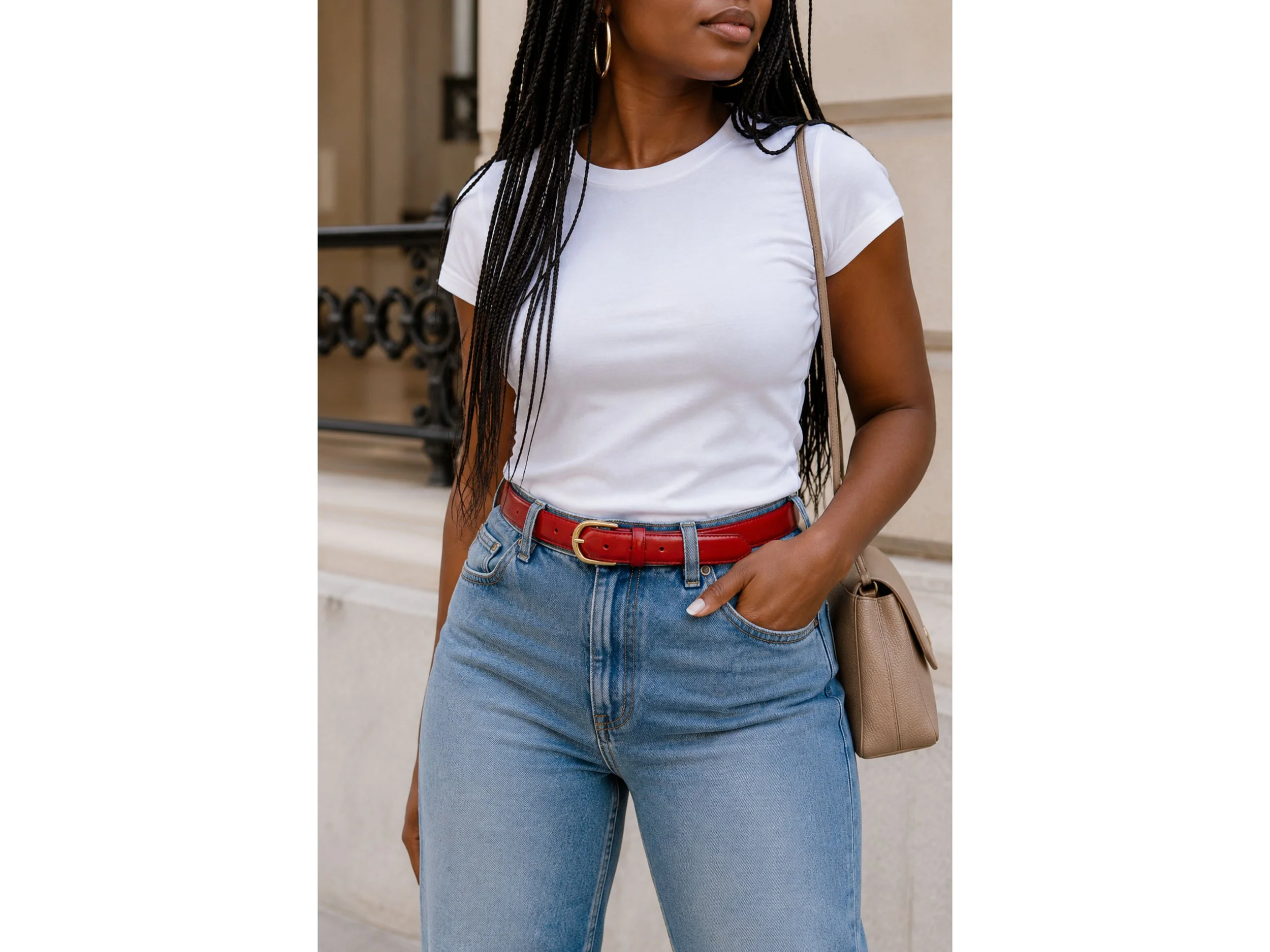 Black woman in a white fitted tee and straight-leg blue jeans styled with a glossy red belt and a neutral shoulder bag.
