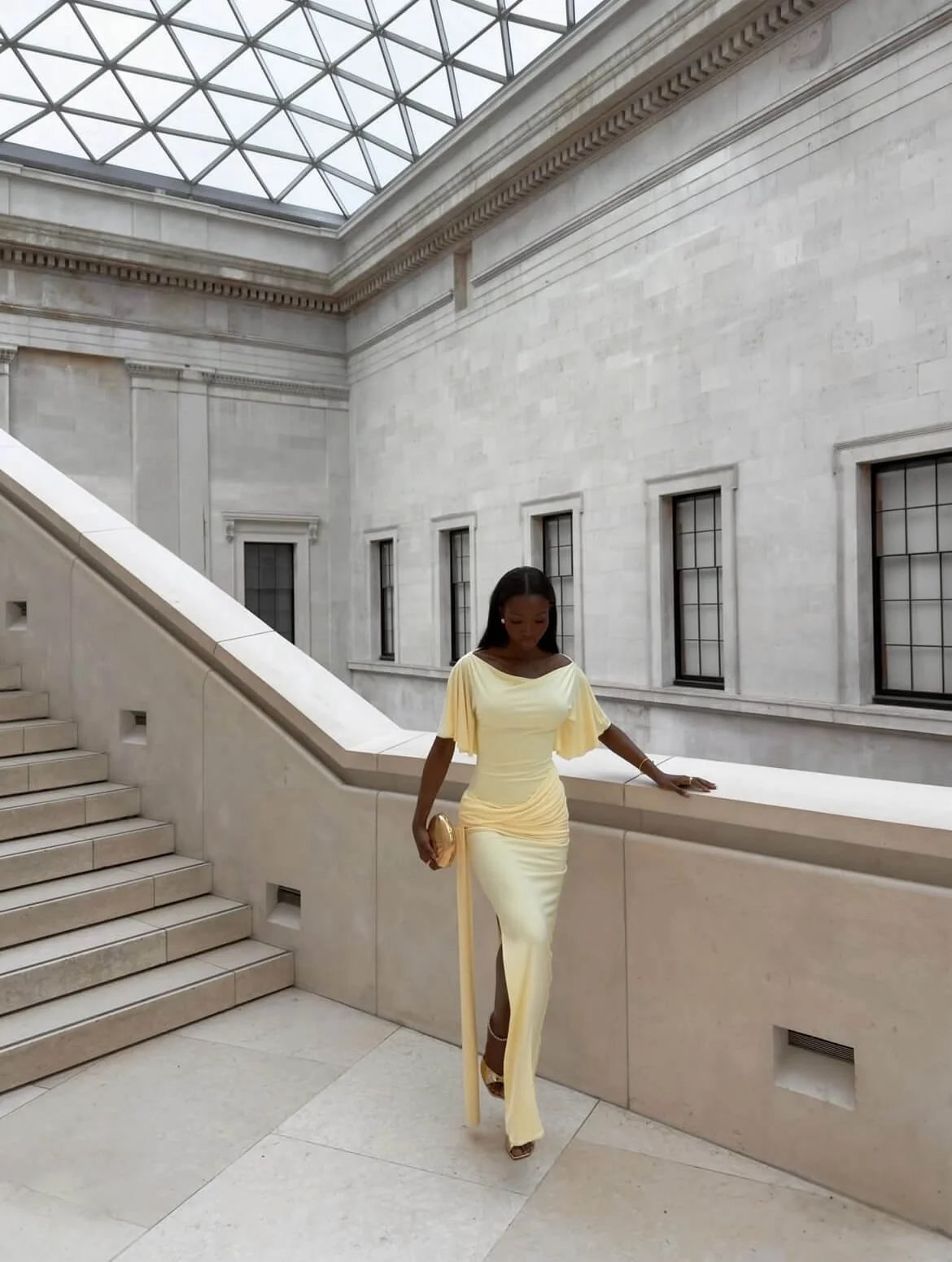 Sia walking in a yellow draped dress with soft sleeves and waist gathering, showing fluid movement and structured silhouette
