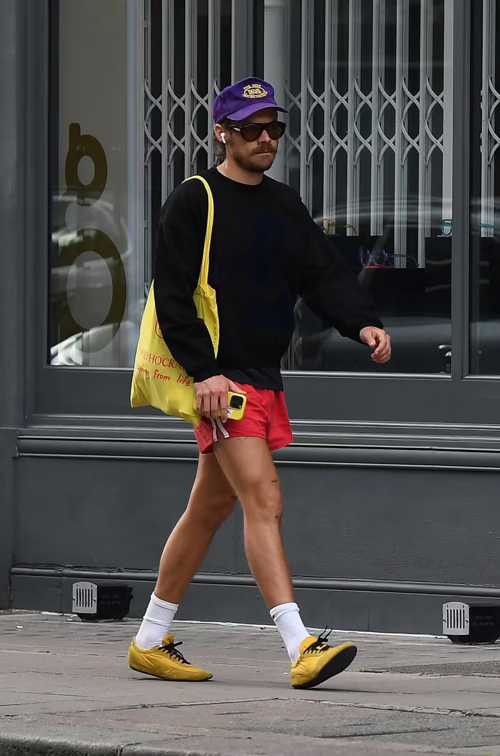 Harry Styles wearing yellow sneakers with red shorts and black sweatshirt