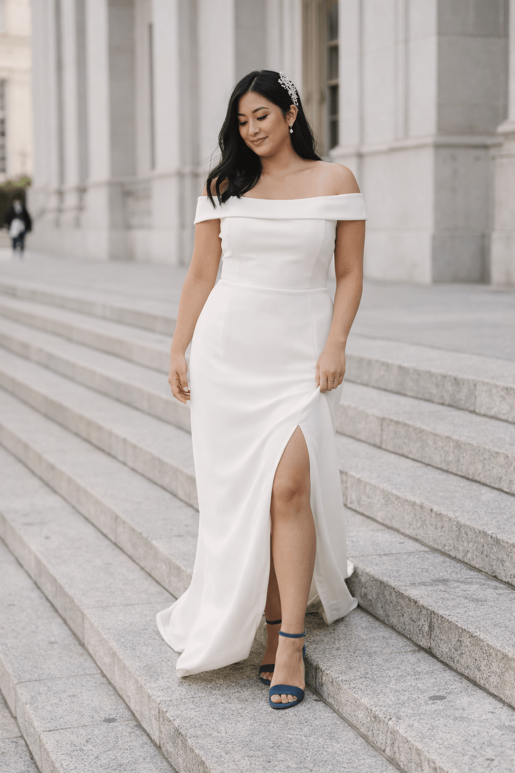 Plus size bride wearing minimal off shoulder column elopement dress walking down city hall steps with blue heels