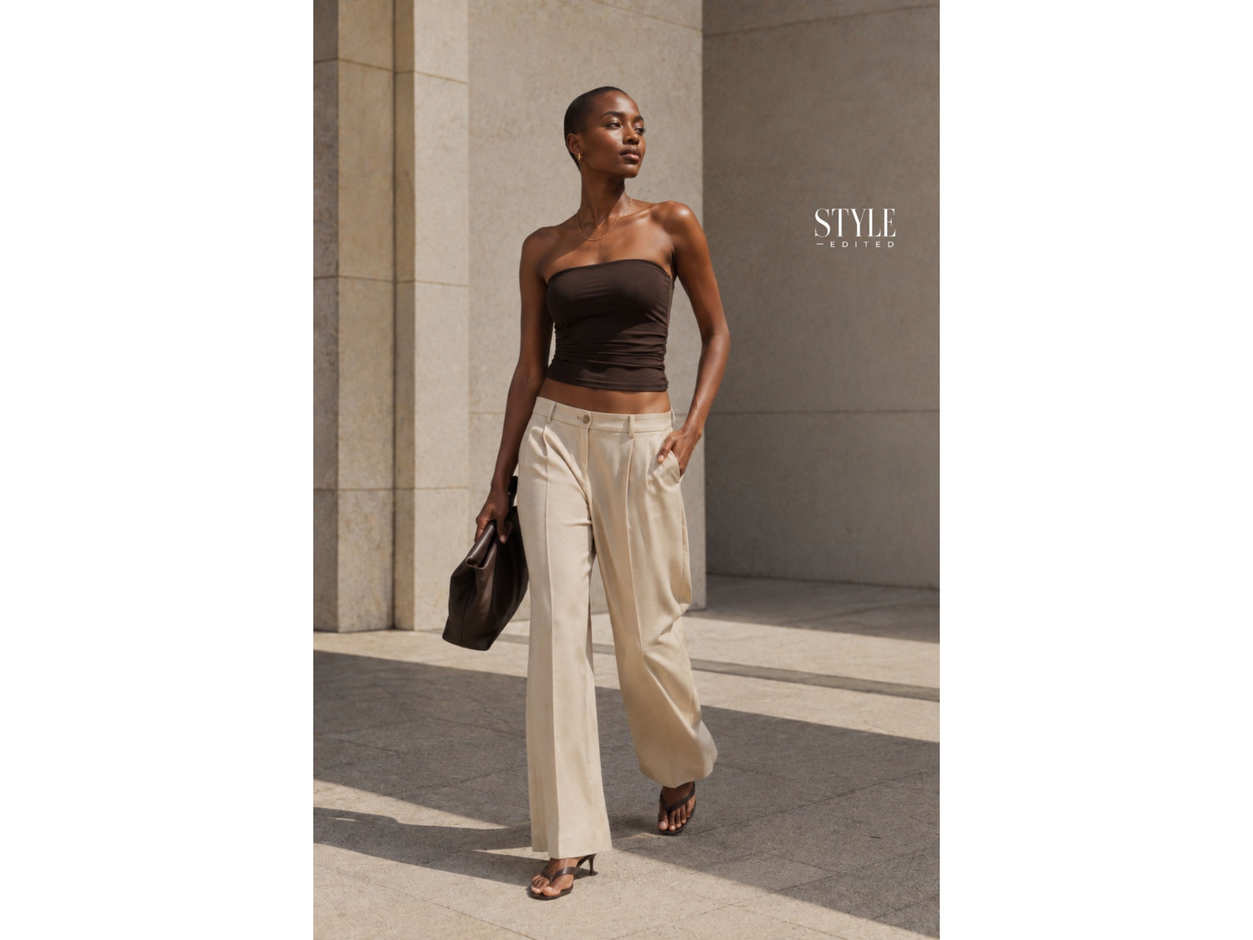 Black woman wearing a fitted tube top with low-rise relaxed trousers and heeled flip-flops in a sleek city setting.