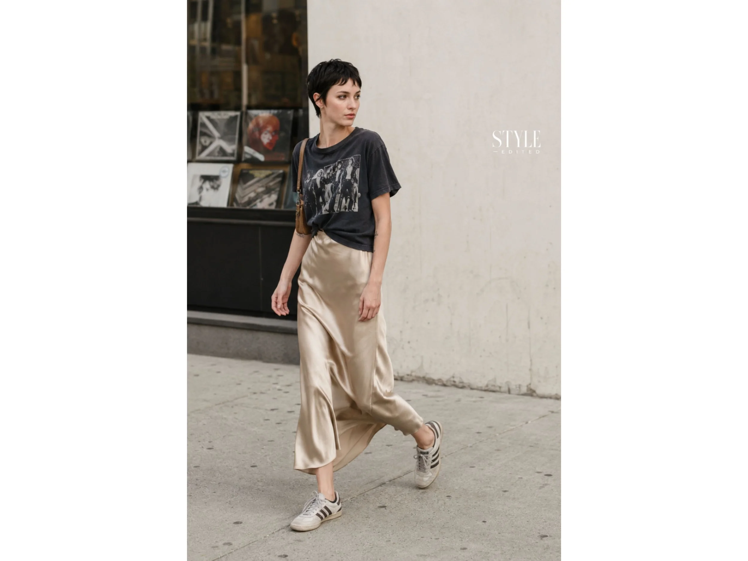 Woman wearing a graphic T-shirt with a fluid slip skirt and retro sneakers on a concrete city block.