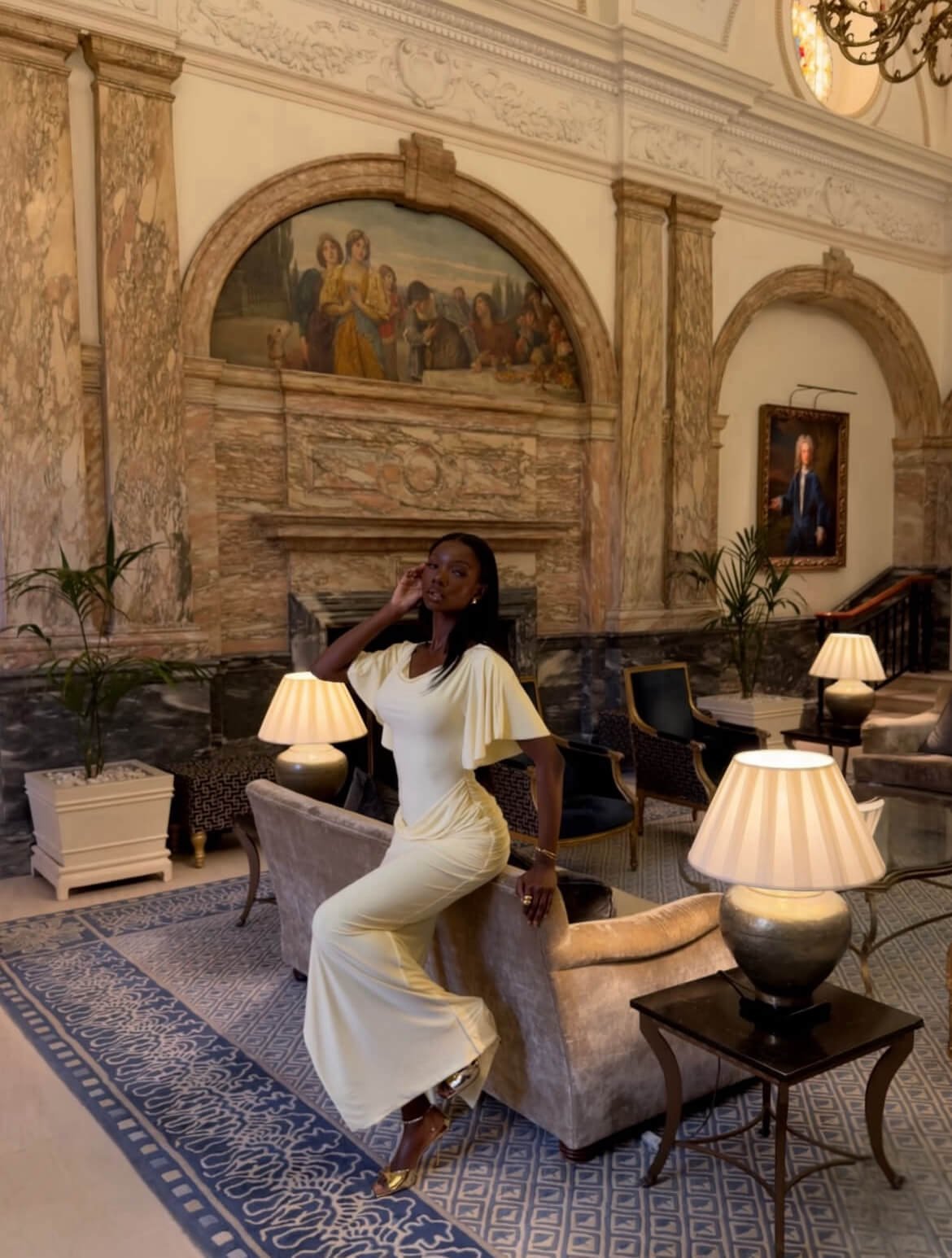 Sia wearing a yellow draped midi dress with soft sleeves, seated in an elegant lounge showing controlled draping and defined waist