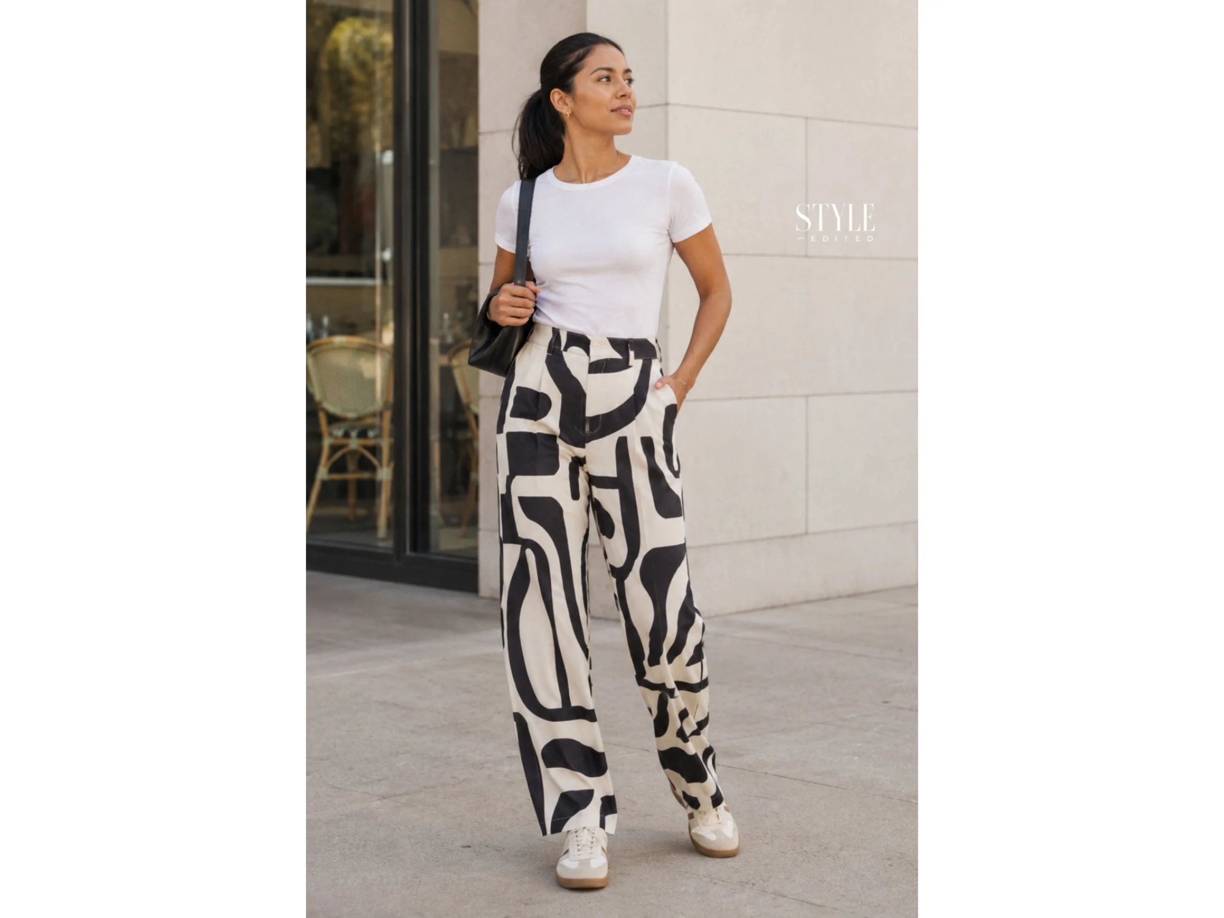 Latina woman wearing bold printed pants with a fitted white tee and retro sneakers on a city sidewalk.
