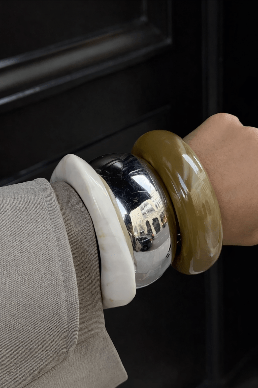 Close-up of Sarah Ndiaye stacked bangles in cream, silver, and olive tones paired with a taupe jacket sleeve