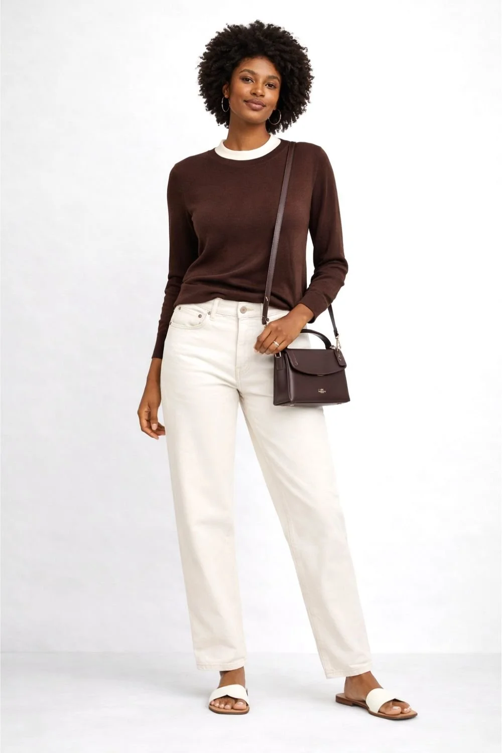 Woman wearing cream jeans with a chocolate brown sweater, flat sandals, and a brown crossbody bag