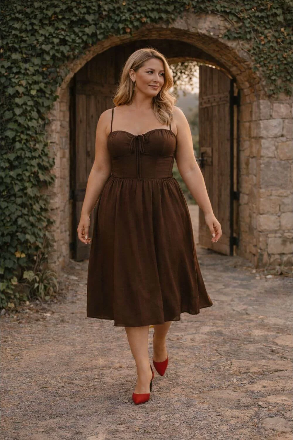 plus size woman wearing brown corset midi dress walking through winery archway