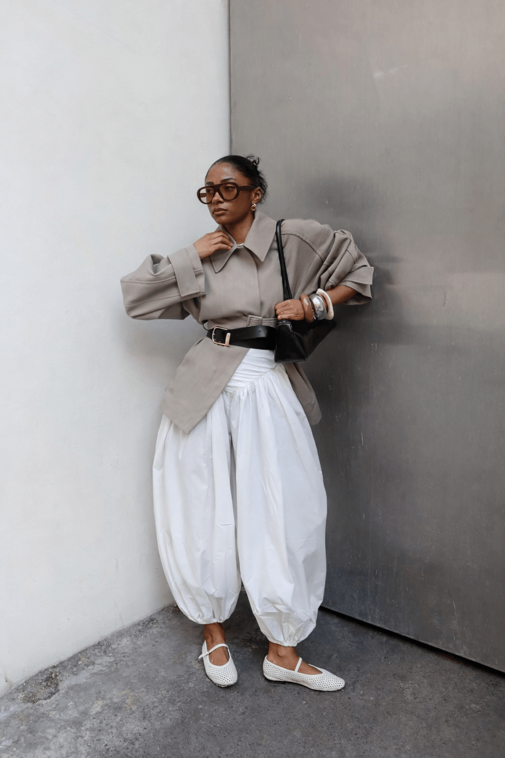 Sarah Ndiaye wearing a belted taupe jacket with exaggerated white balloon trousers, mesh flats, and stacked bangles emphasizing structured volume