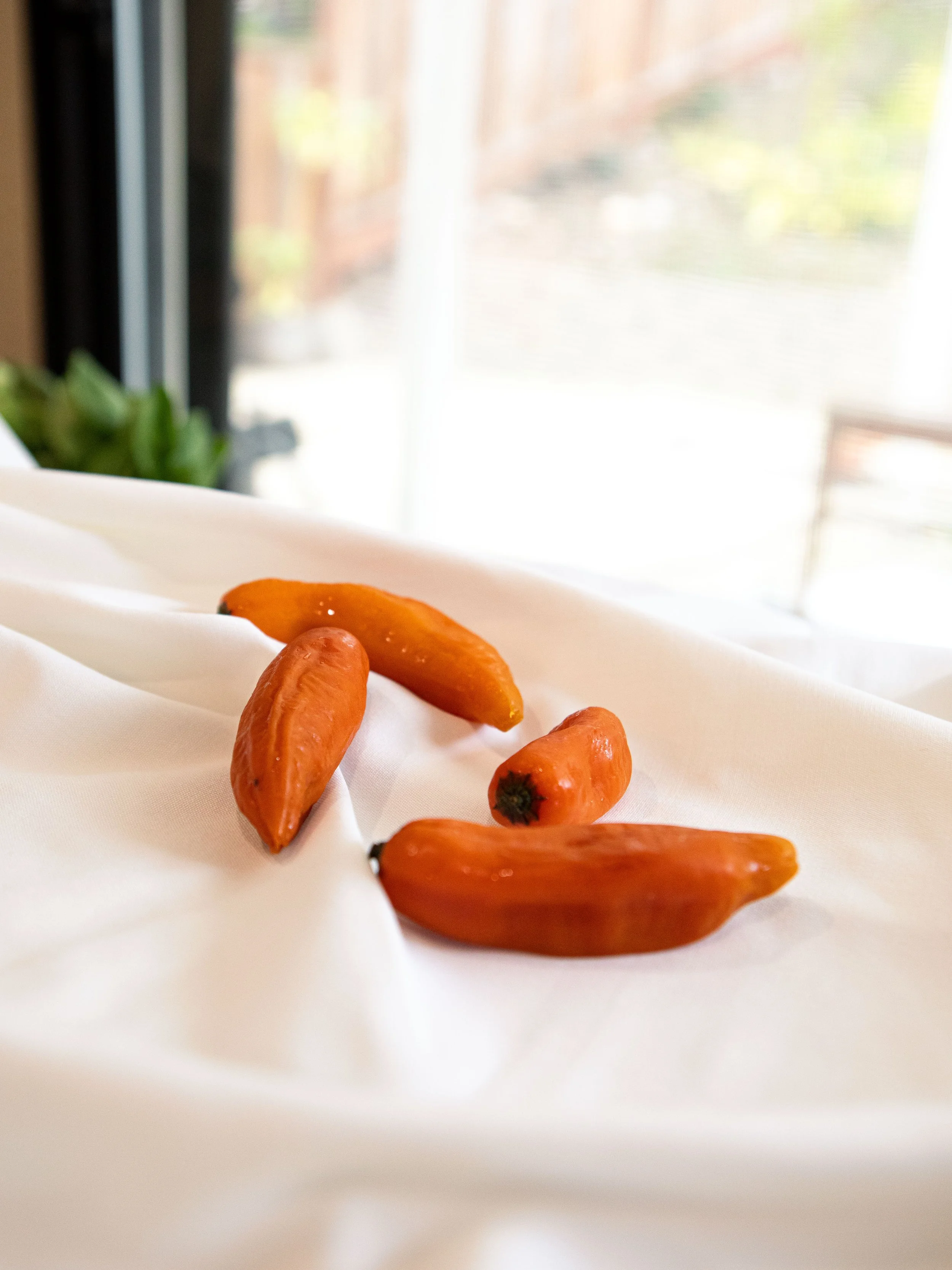 Small orange ceramic peppers on white fabric near a window.