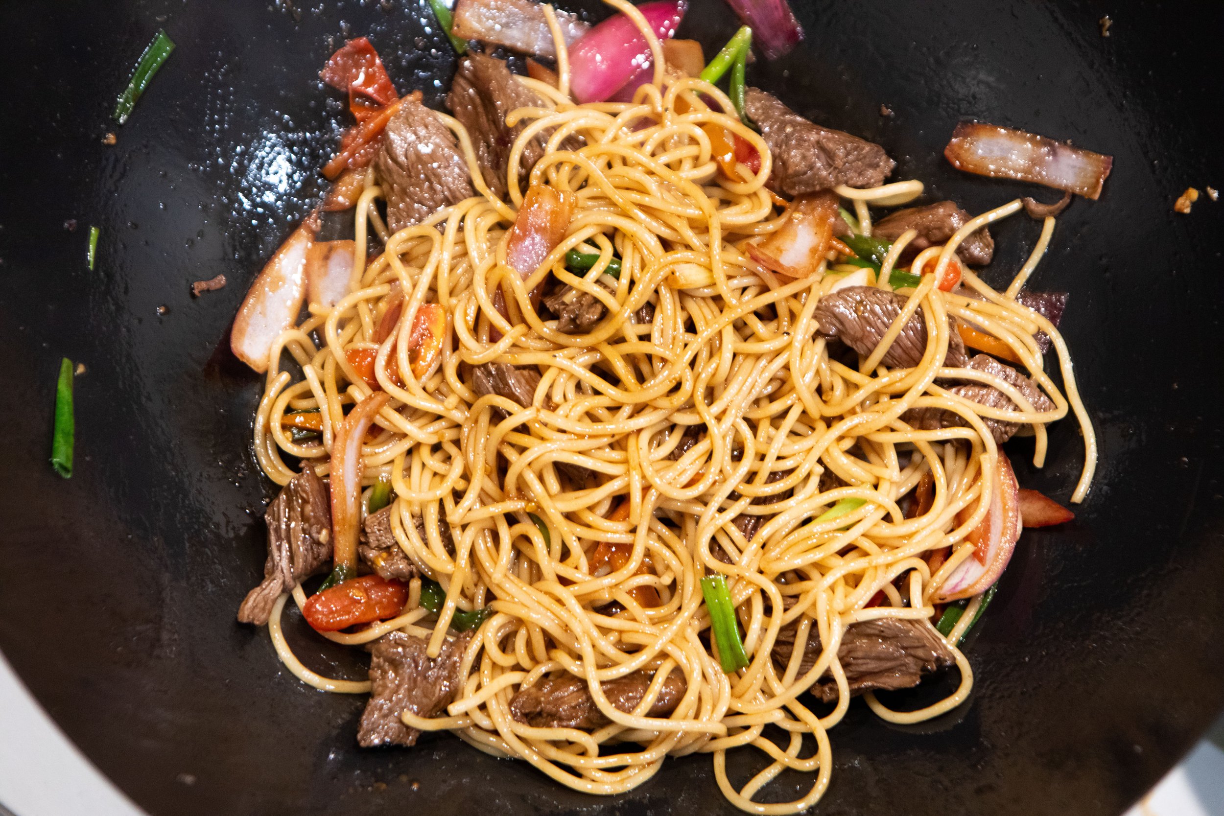 Cooked stir-fry noodles with beef, vegetables, and sauce in a wok.