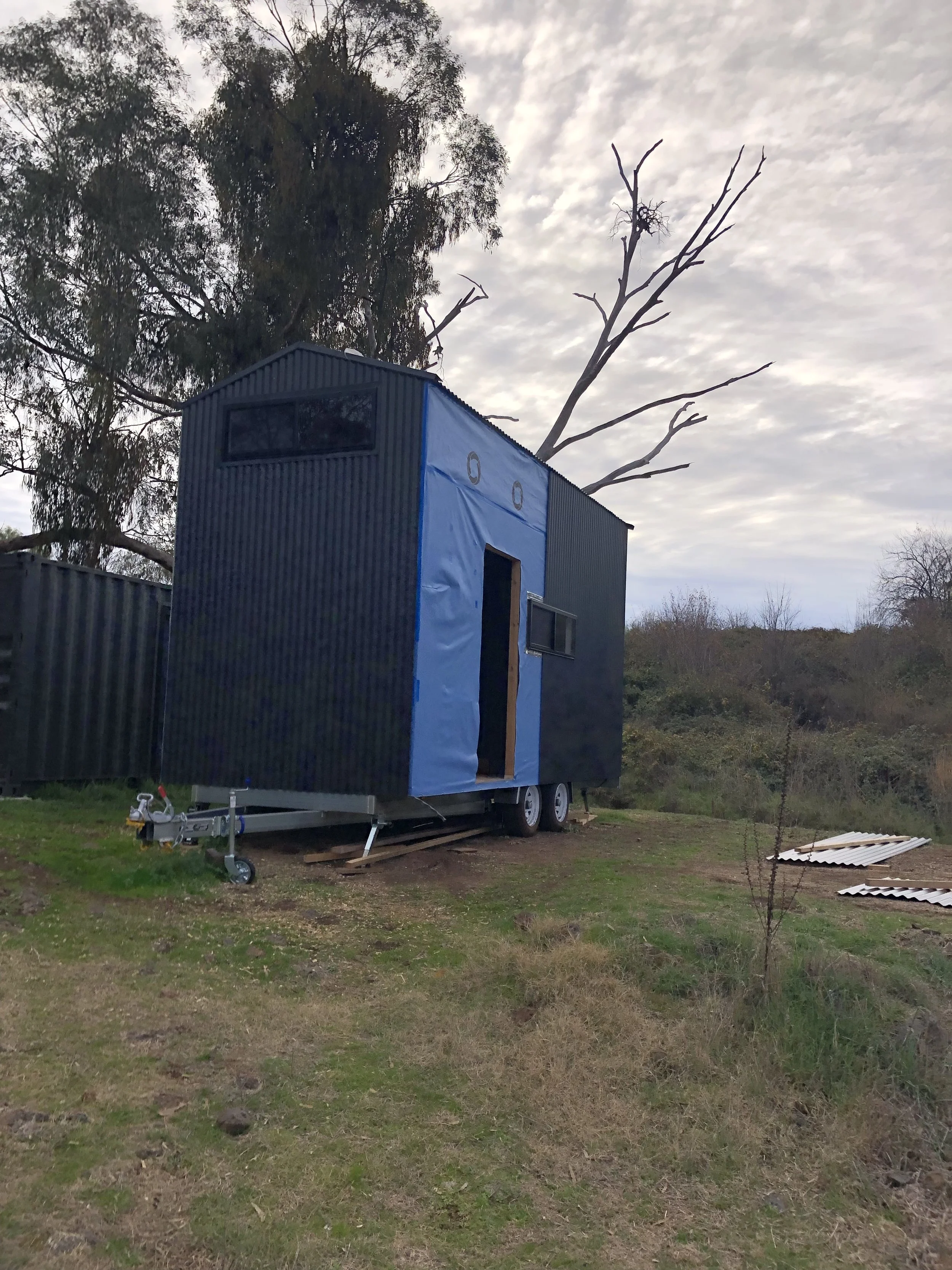 A tiny house on wheels under a cloudy sky with trees in the background.