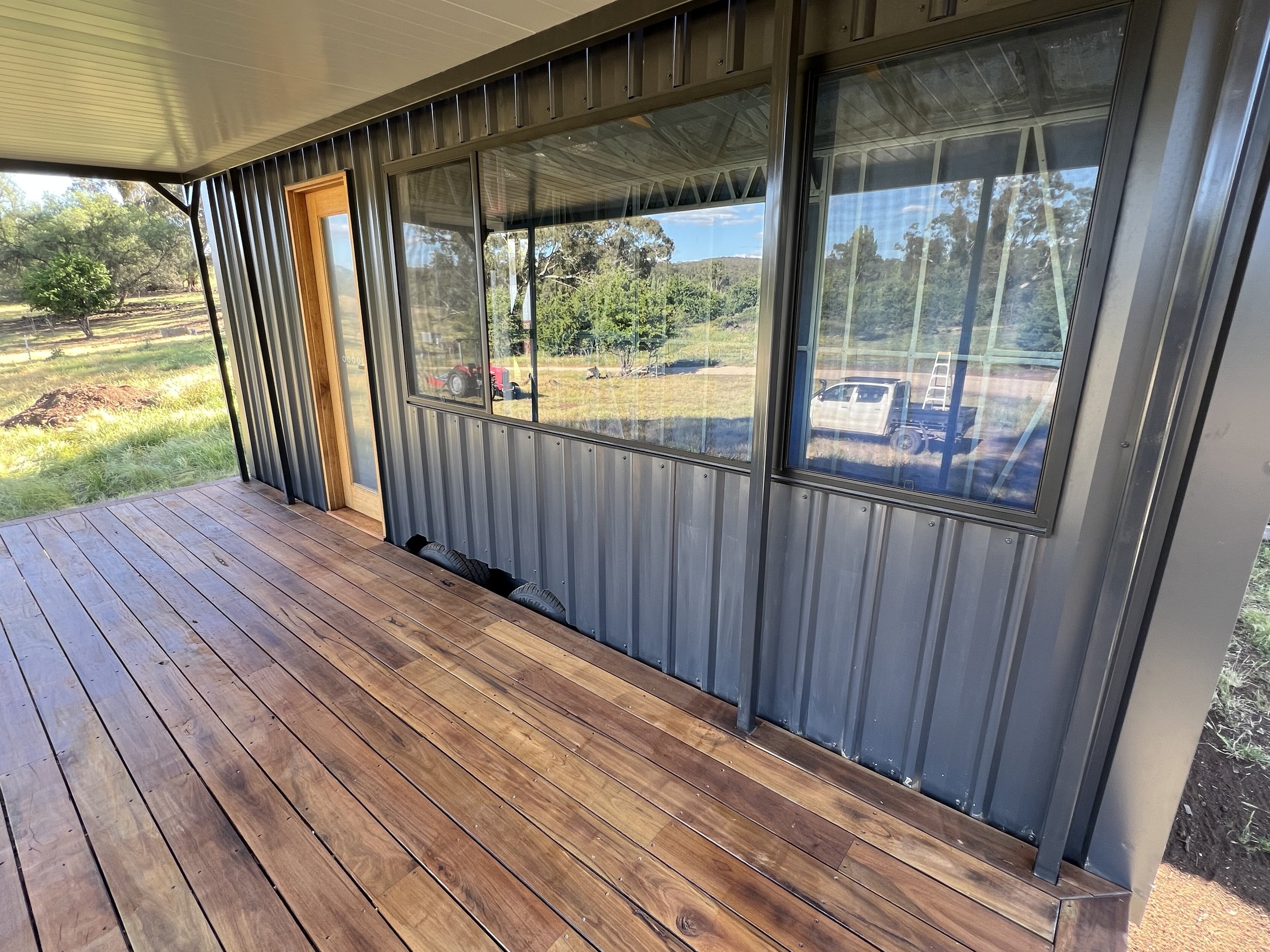 Porch with wooden floorboards and metal siding, large window reflecting scenic outdoors, and a door with glass panel.