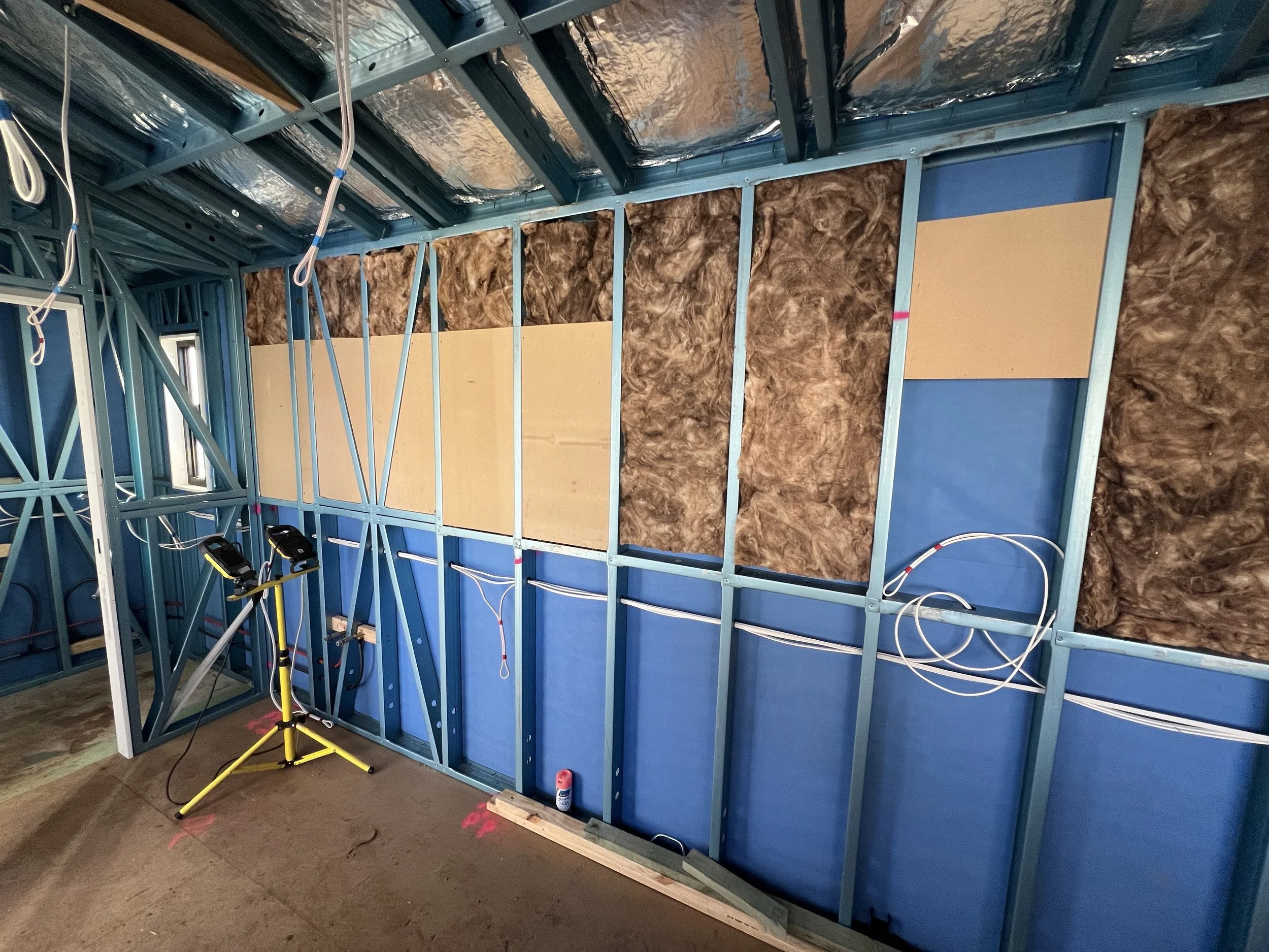 Interior of a building under construction, showing blue steel framing, wall insulation, and electrical wiring.
