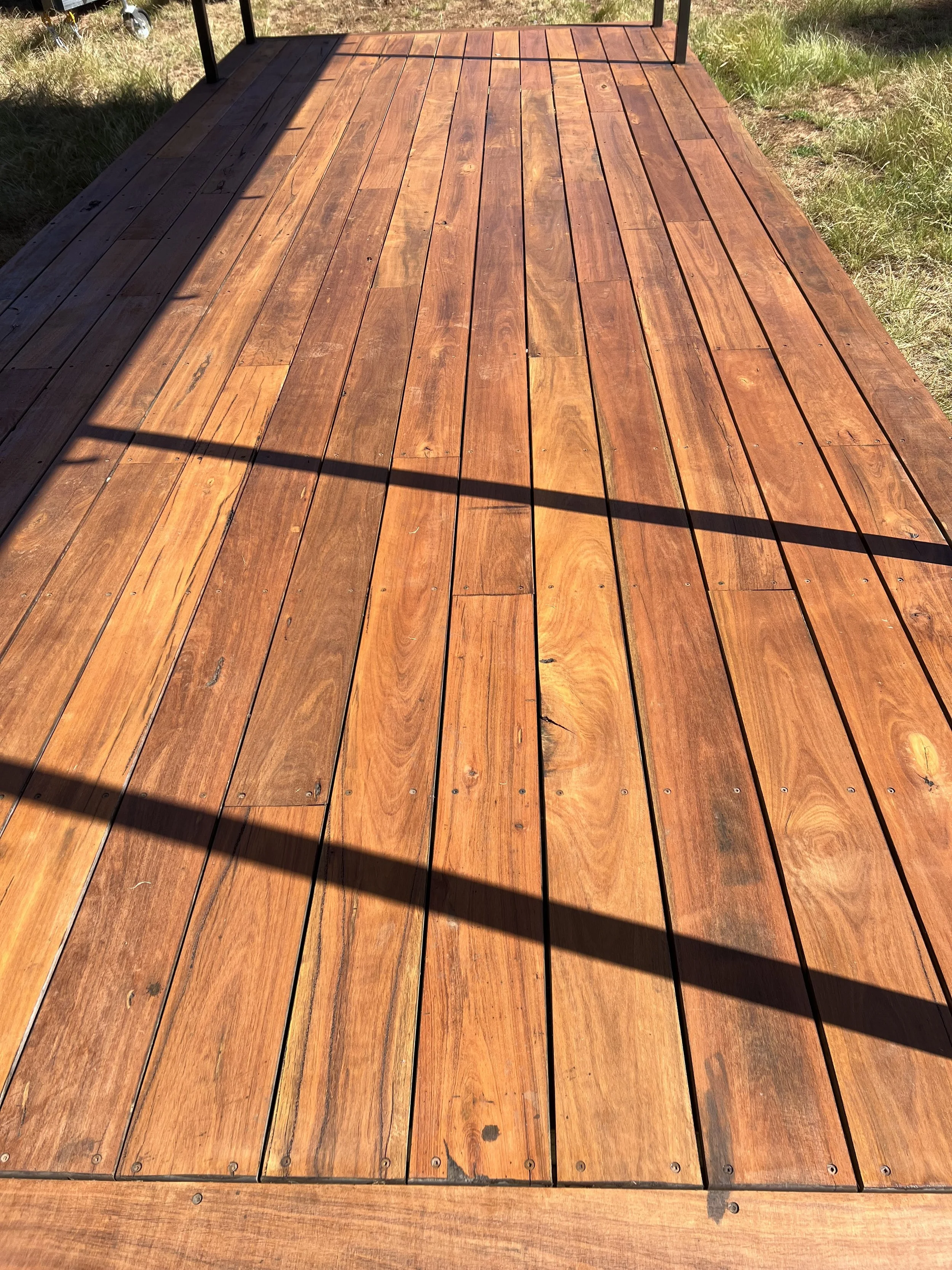 Close-up view of a wooden deck outdoors, with grass and sunlight.