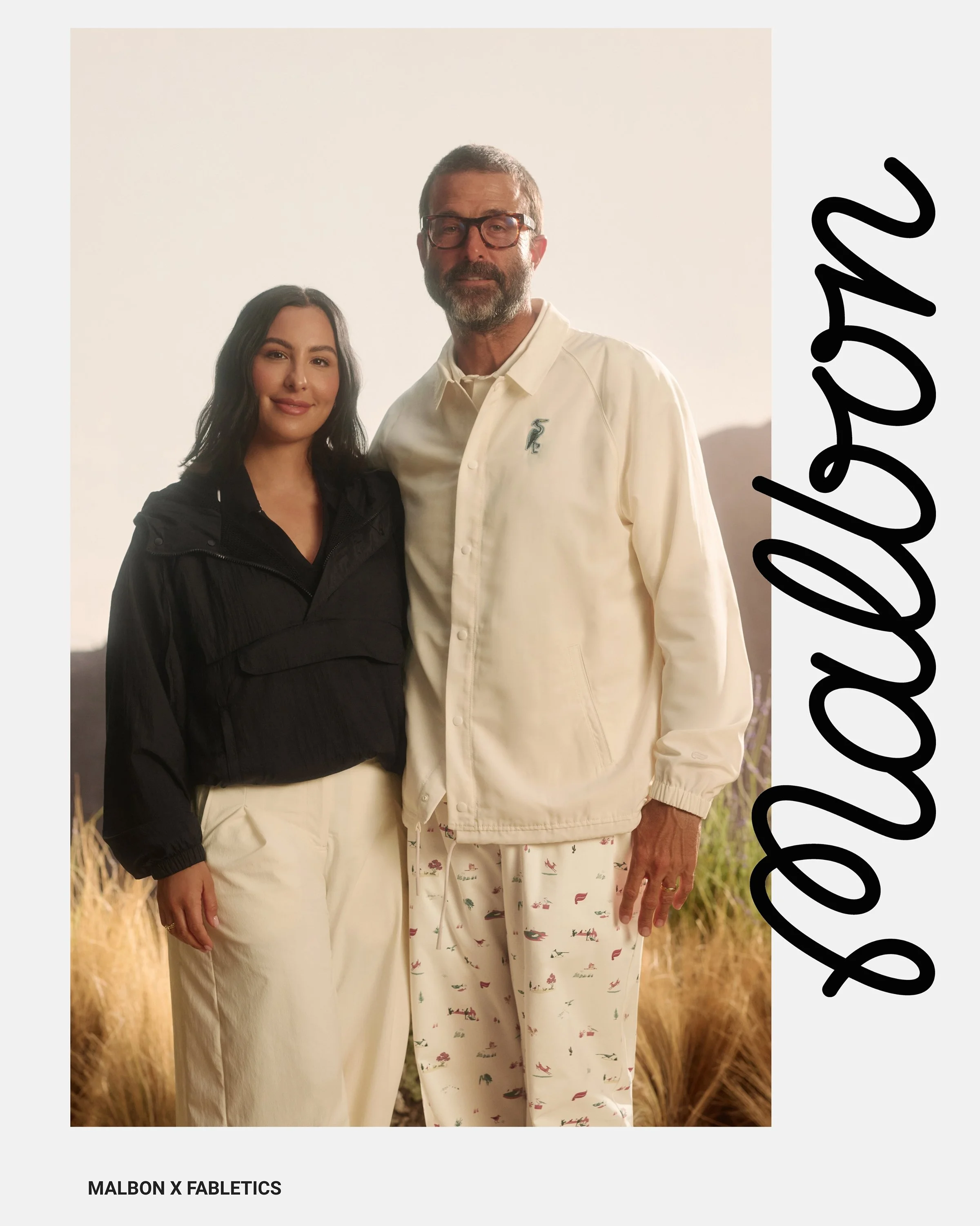 Malbon founders standing outdoors, both dressed casually, with a mountainous landscape in the background. 