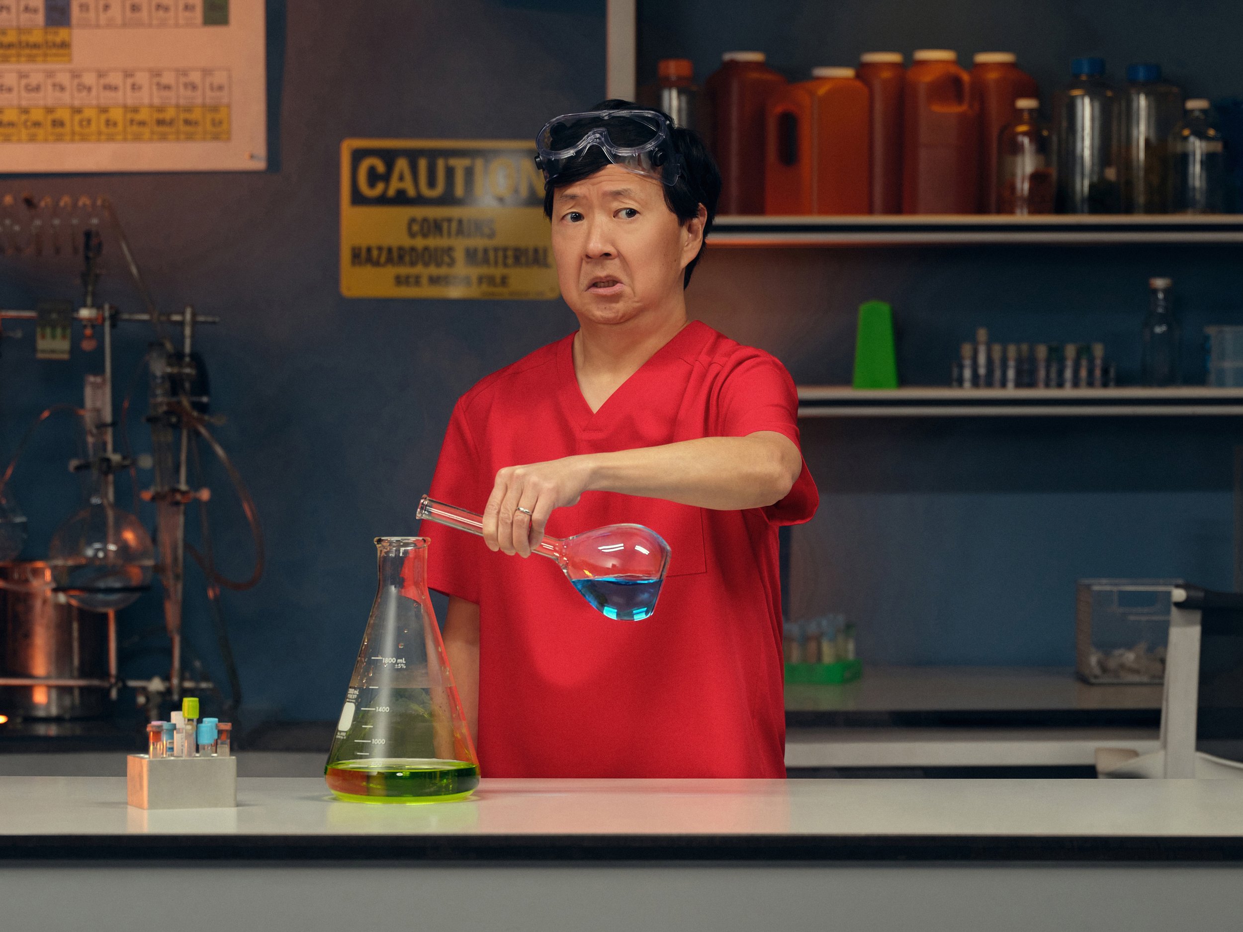 Man wearing red shirt and safety goggles mixing chemicals in laboratory.