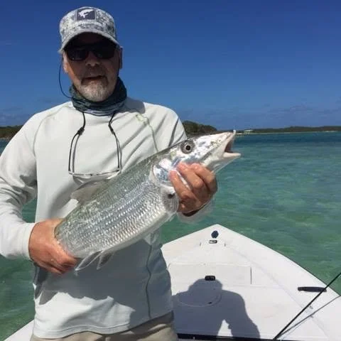 Man in sunglasses and hat holding a large fish on a boat in clear blue water
