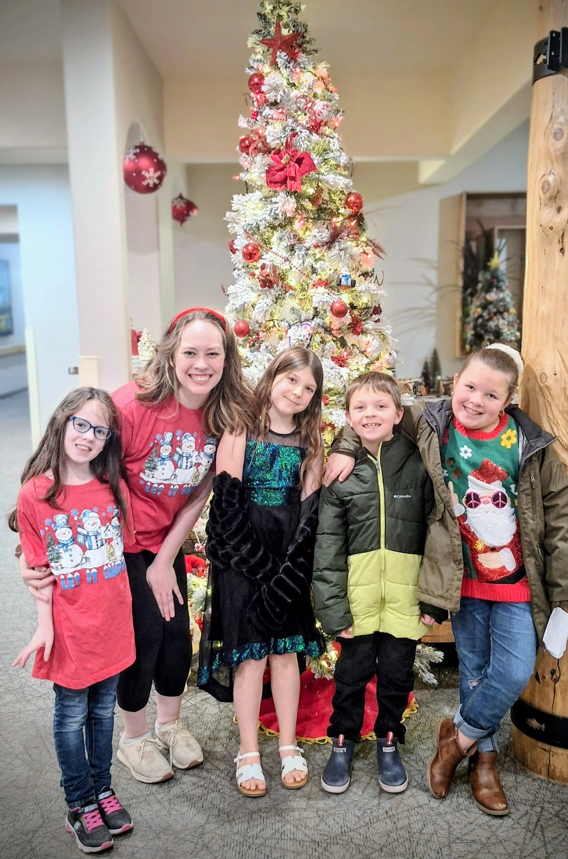 A group of five children and one adult girl standing in front of a decorated Christmas tree.