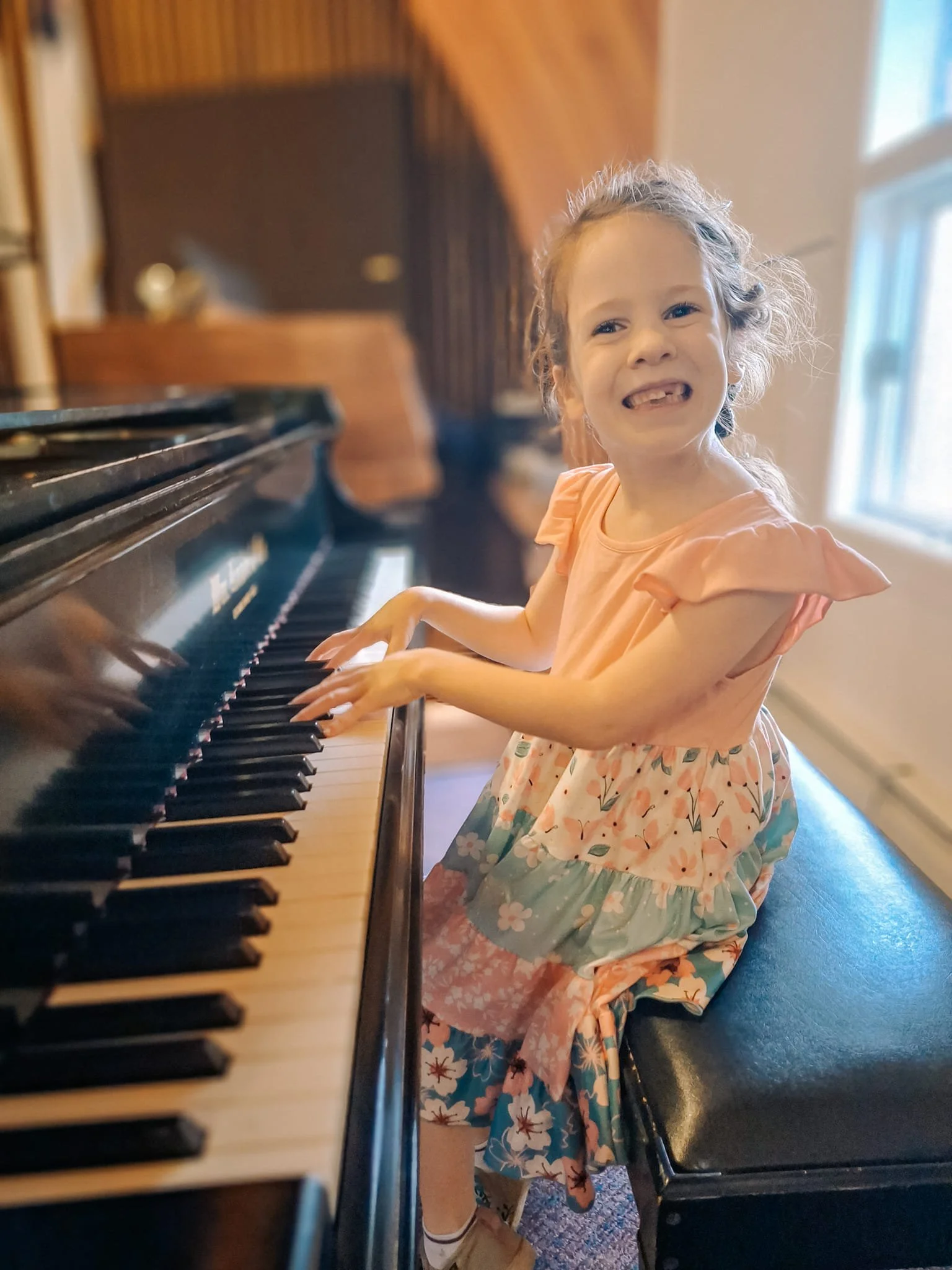 A young girl with curly hair smiling and playing the piano in a cozy room.