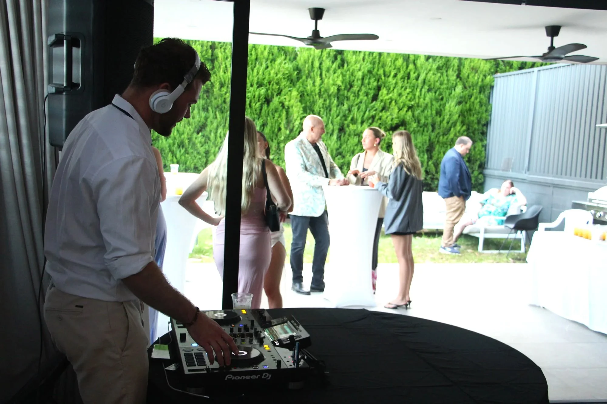 DJ in headphones playing beside a garden terrace as engagement party guests mingle