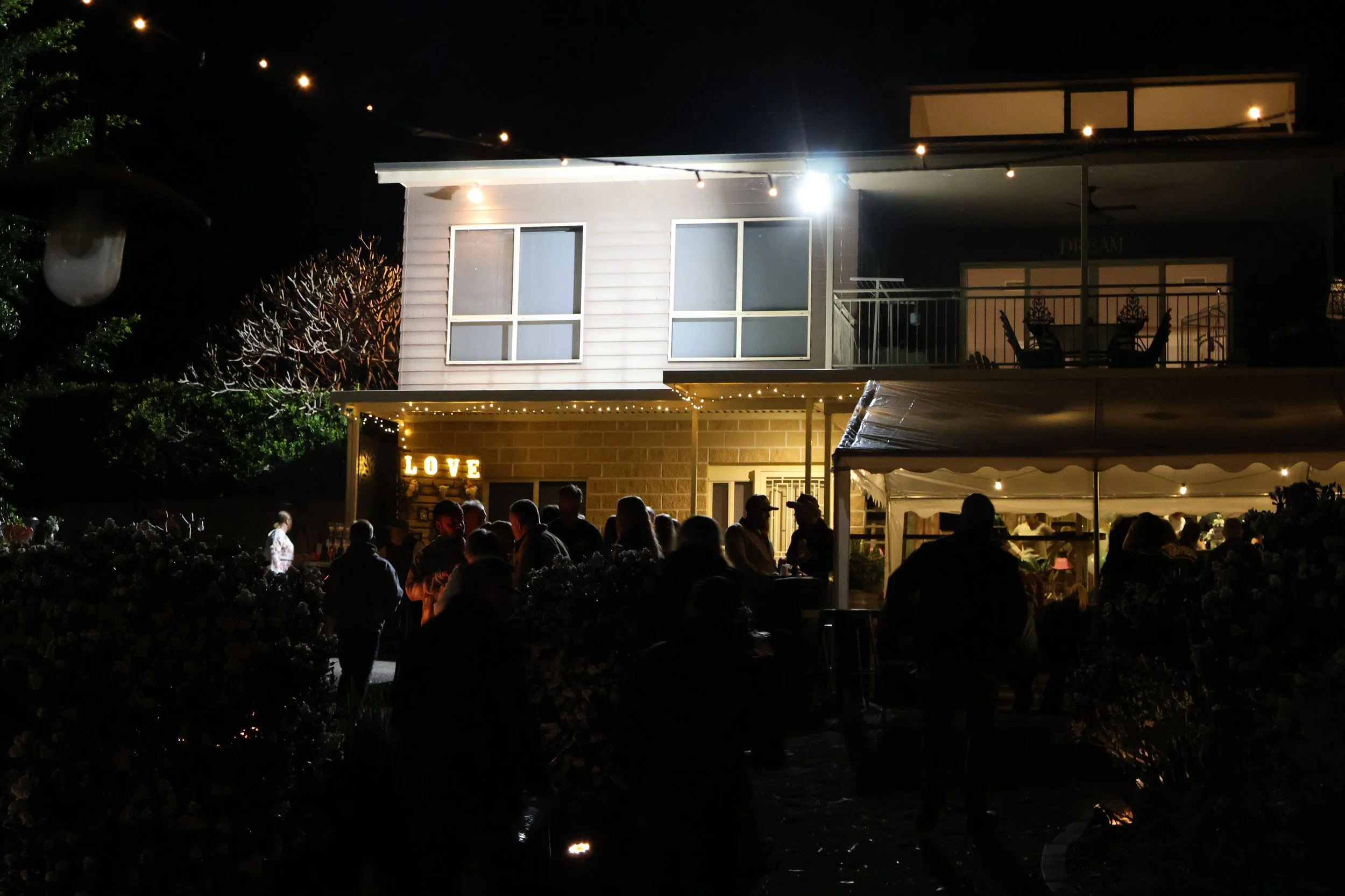 Guests gathered outside a lit-up house at a rural engagement party at night