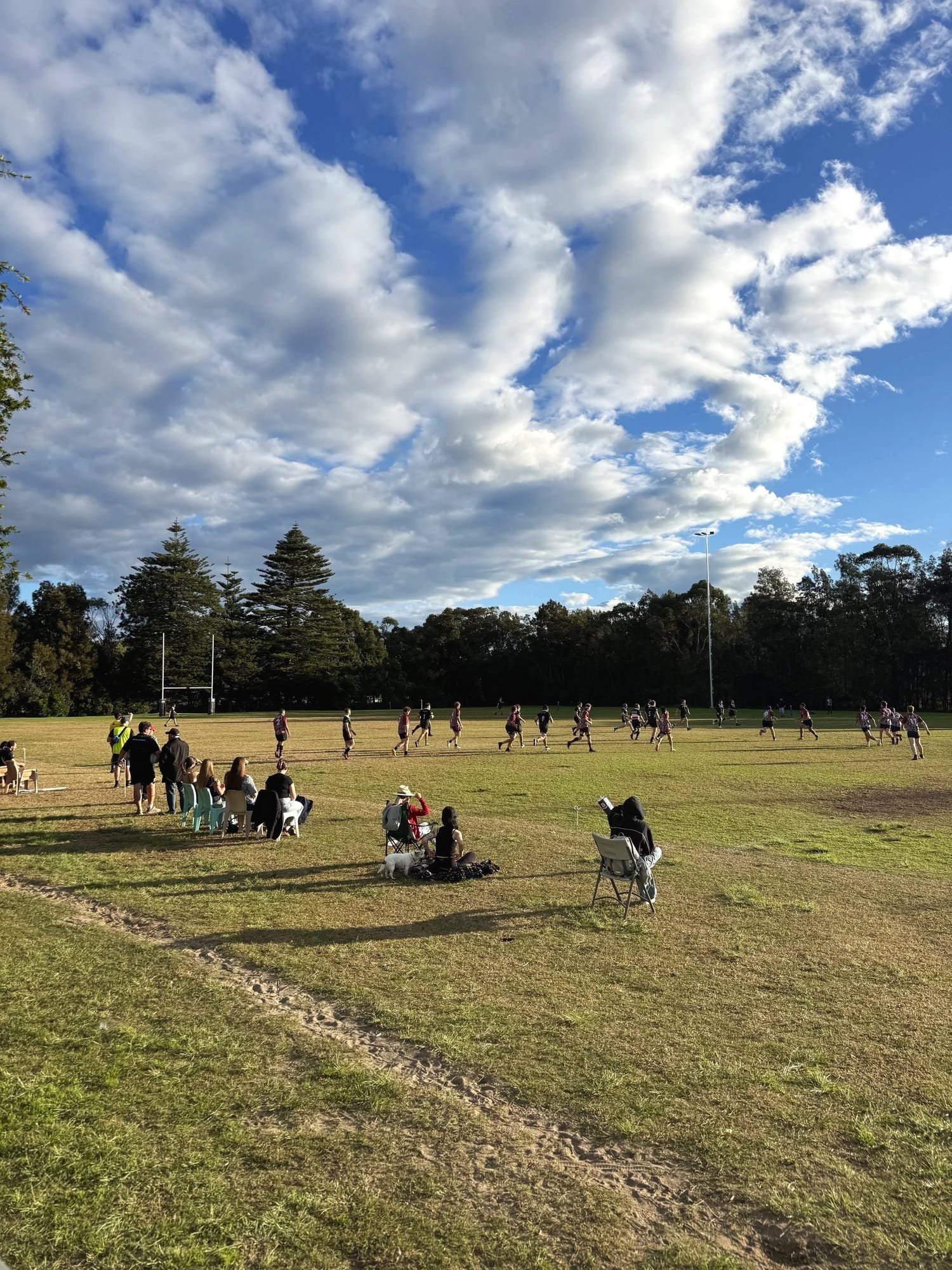 Spectators watching a Latin Round rugby game on a sunny field under blue skies