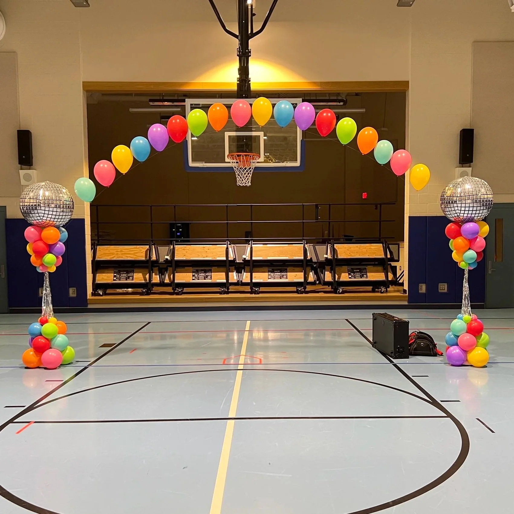 Bright rainbow color balloons creating a floating helium arch for a school dance