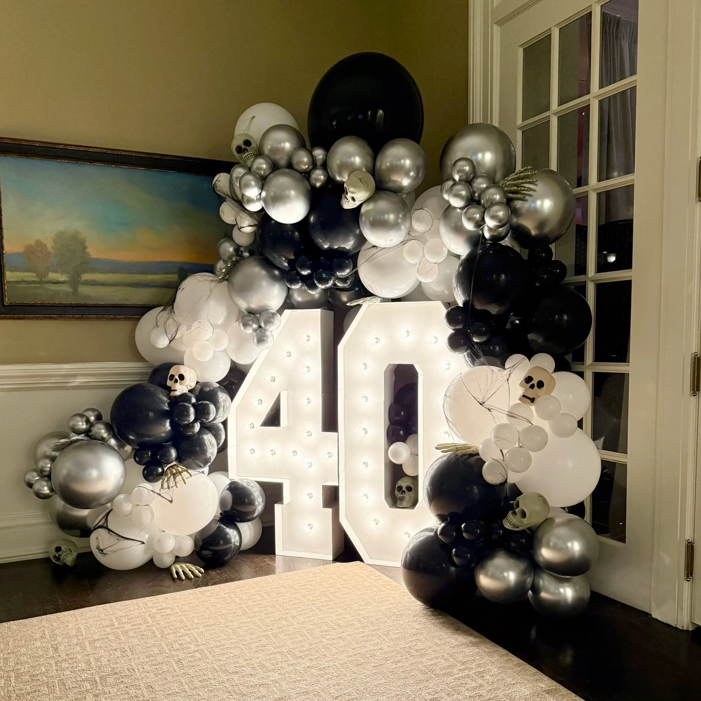 Decorative Halloween display with large illuminated number 40, surrounded by black, white, and silver balloons, skulls, and skeleton hands.