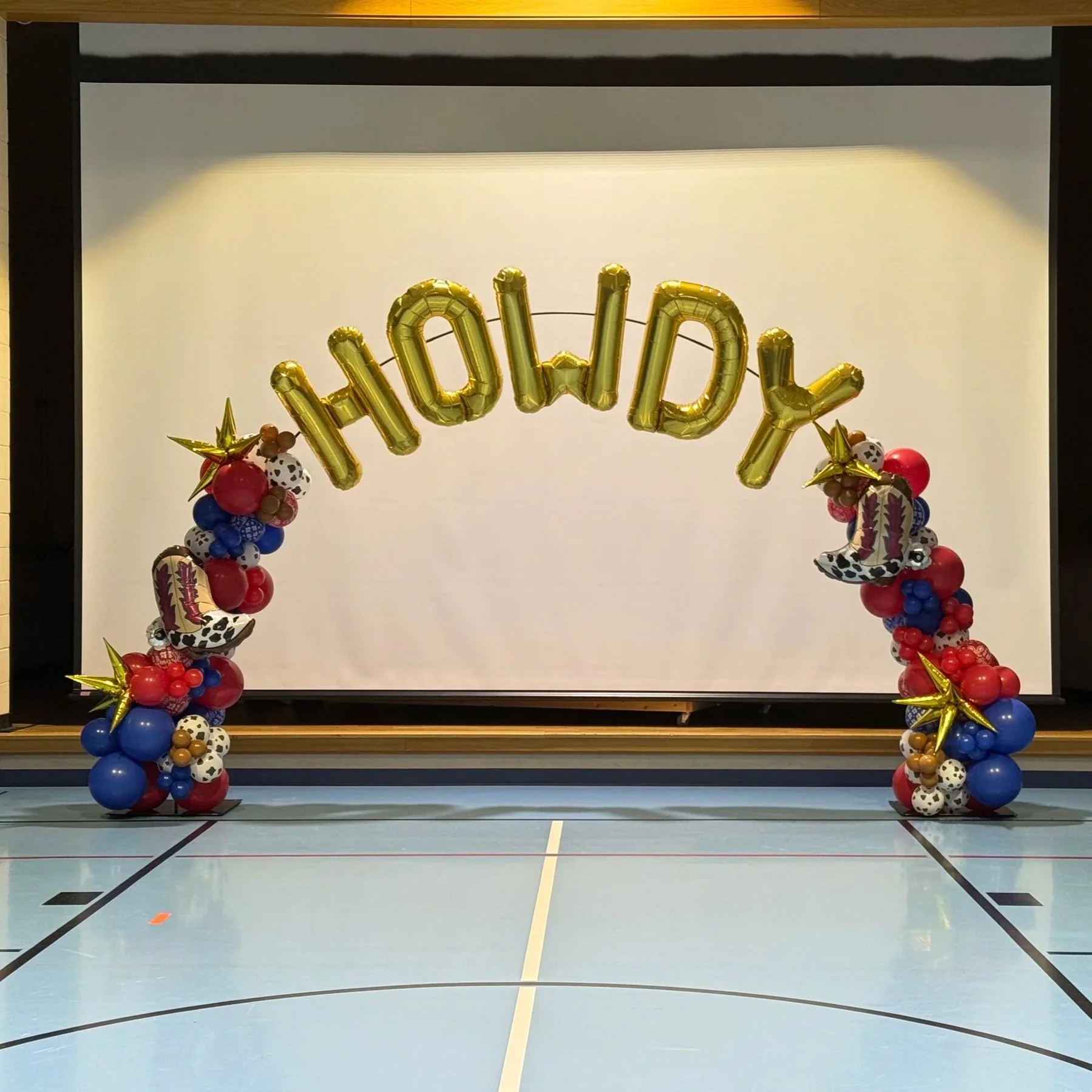 Balloon arch with gold letters spelling 'HAPPY' on a sports court.