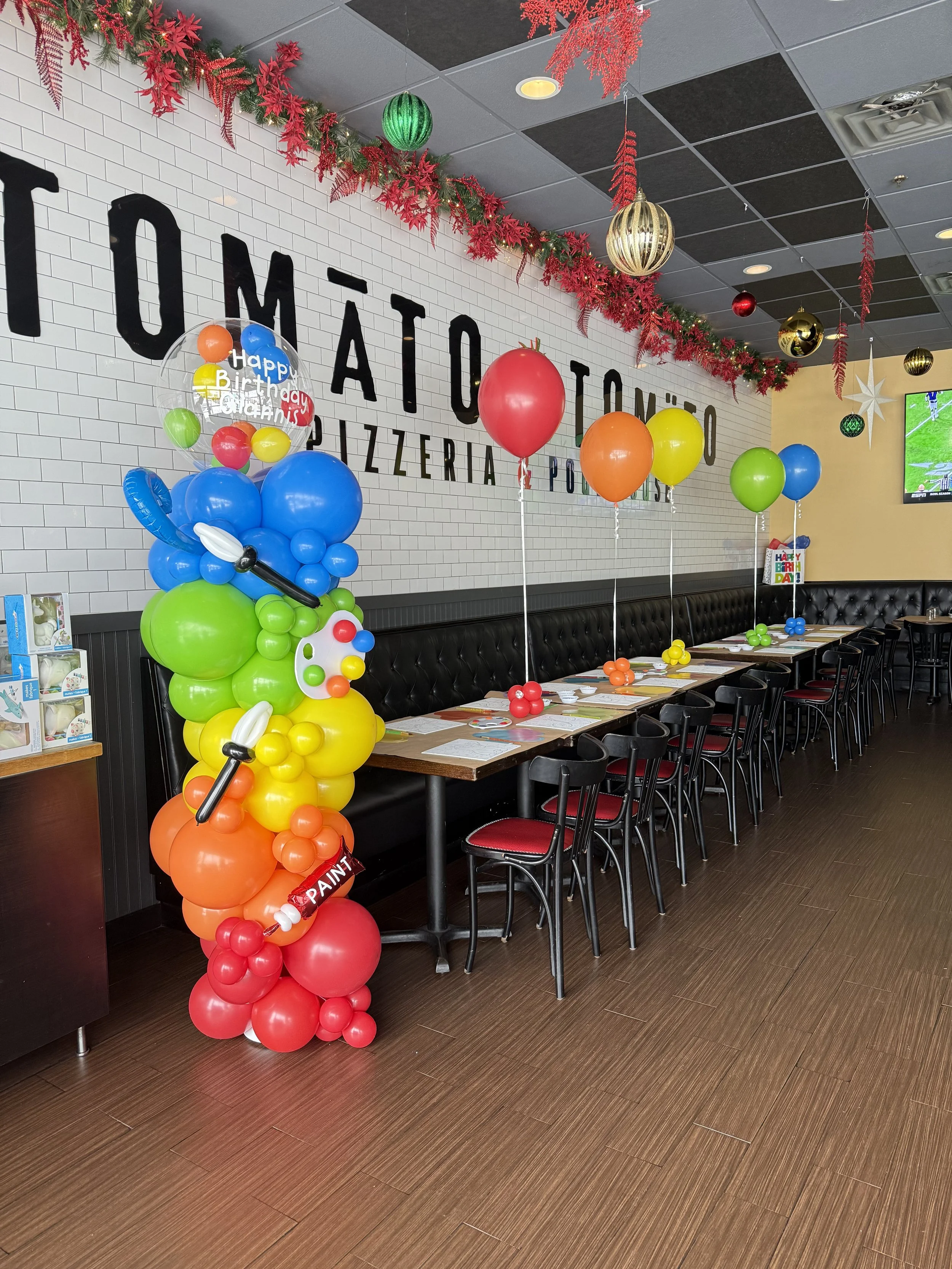 Decorated restaurant with colorful balloons, red and green garlands, and festive ornaments for a birthday celebration.