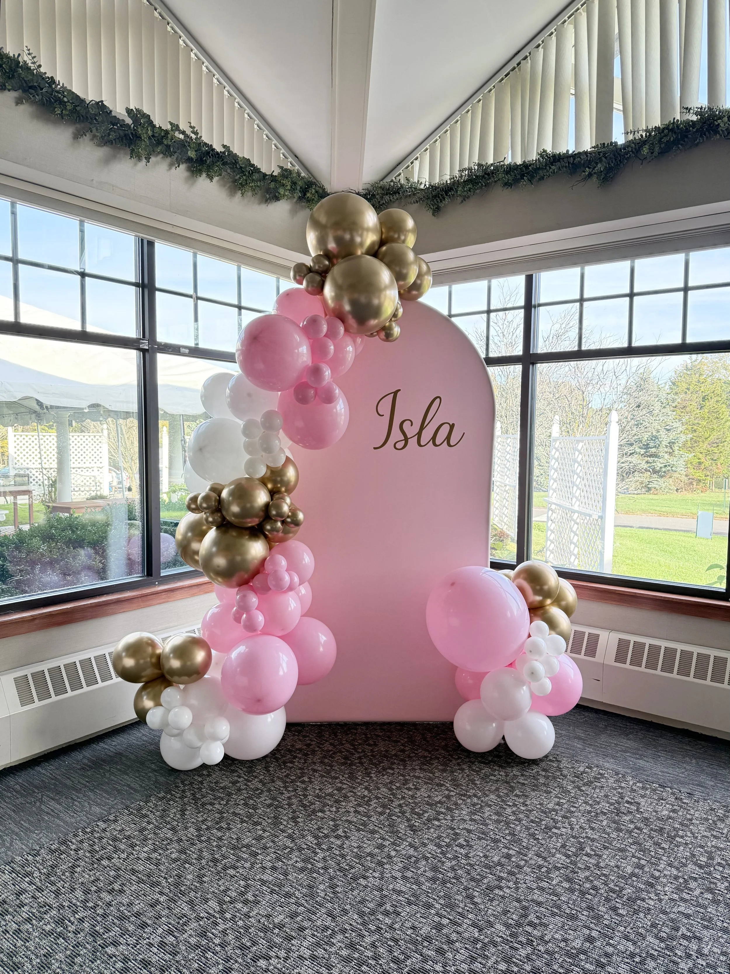 White, pink and gold balloons accent a light pink backdrop personalized with Isla name for a baptism celebration at Tashua Knolls in Trumbull CT.