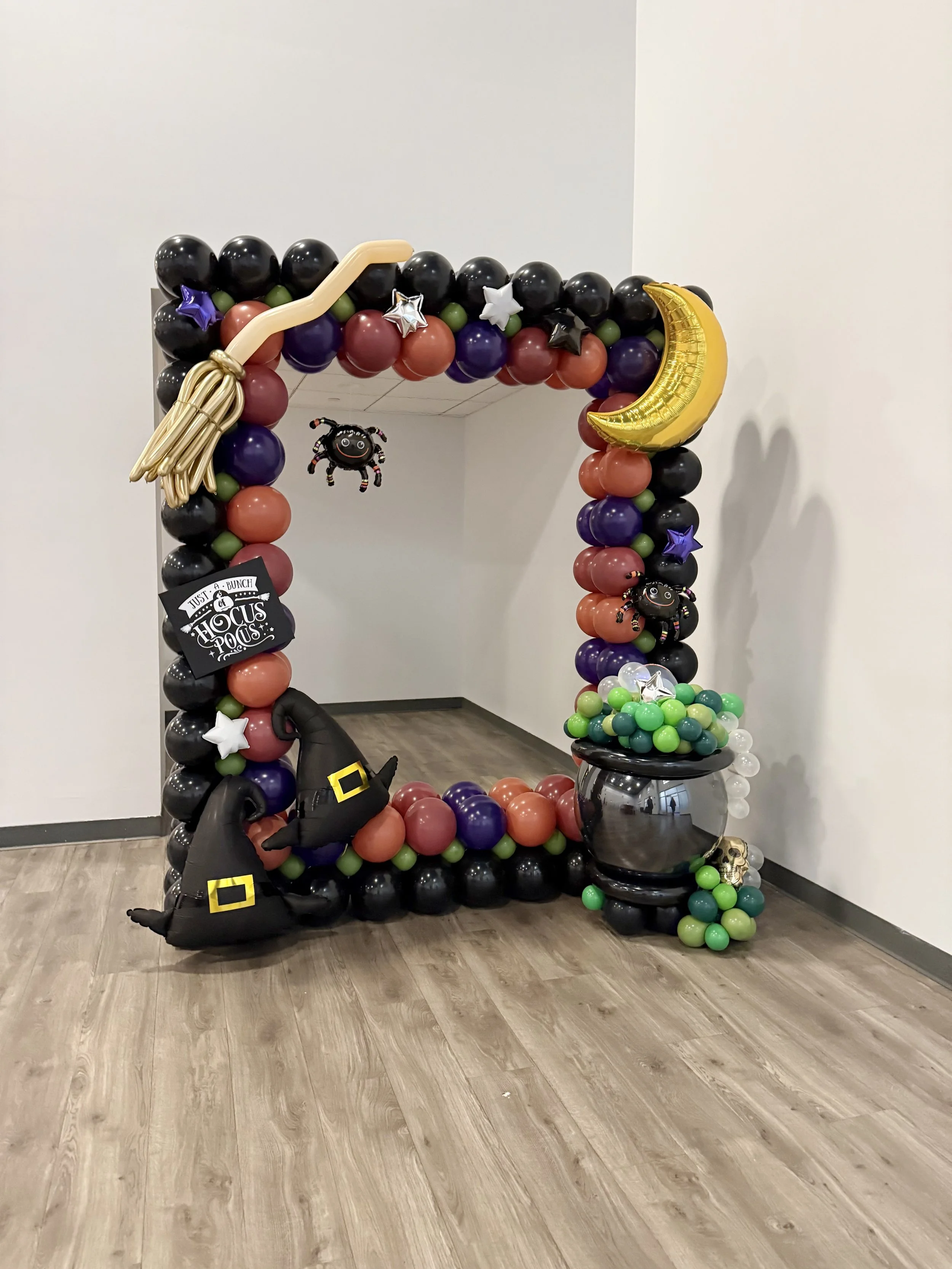 Balloon Halloween decoration with black, orange, purple, and green balloons, featuring a witch hat, broomstick, moon, stars, spiders, and a cauldron.