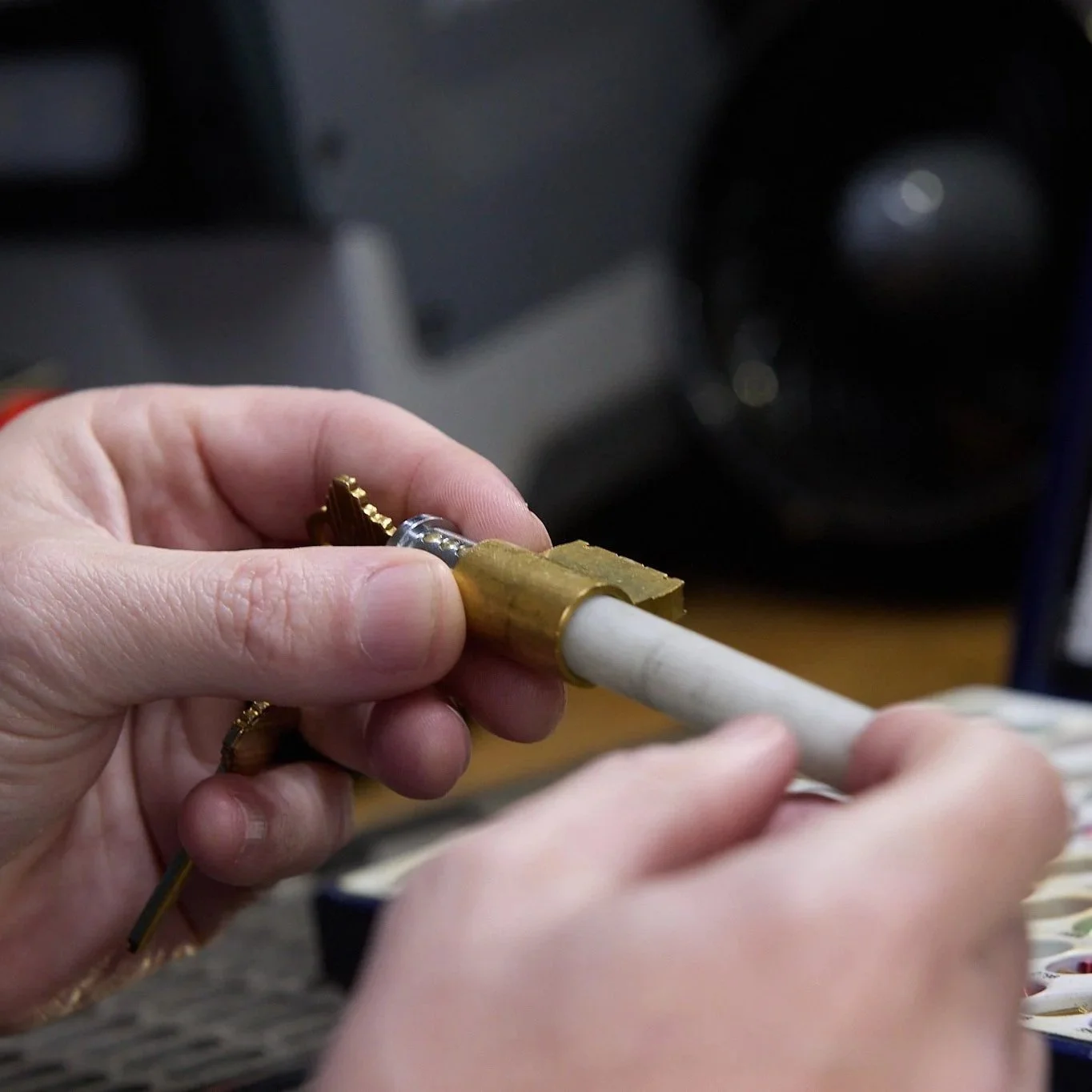 Hands inspecting a brass file cabinet cam lock and key cylinder, showing wear and mechanical stress that can cause jamming or failure.