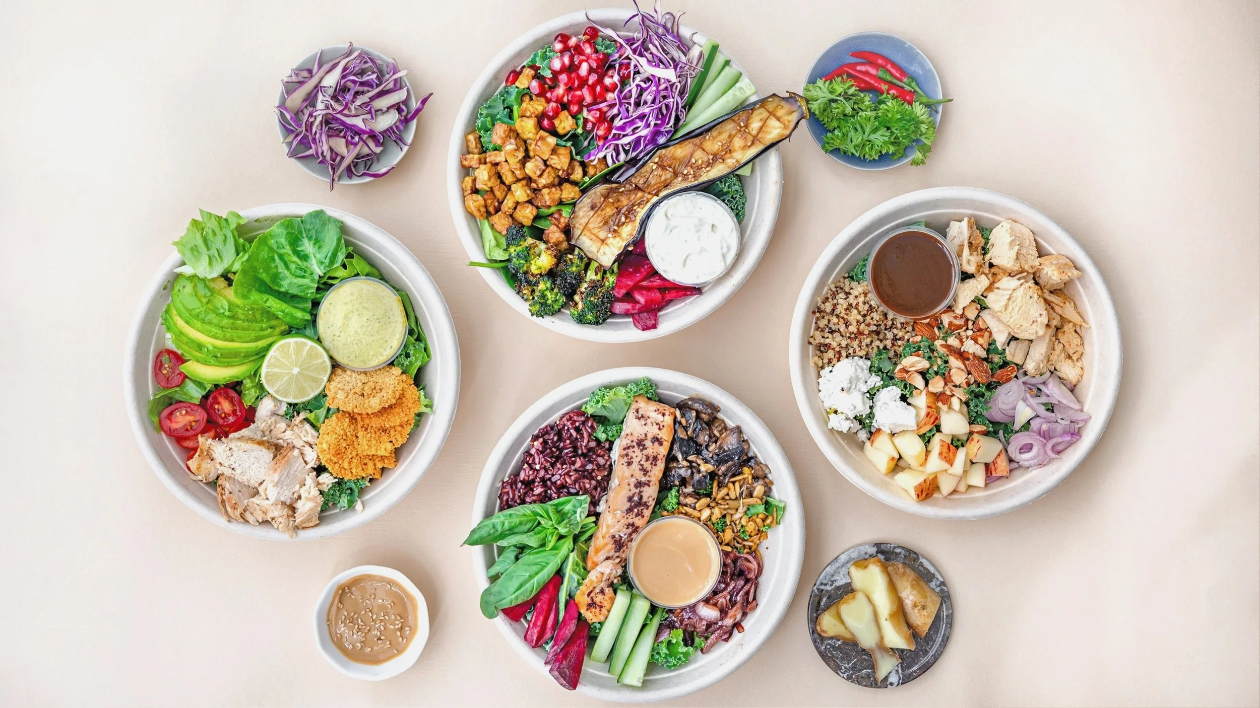 Assorted healthy dishes featuring salads, vegetables, and grains, served in white bowls on a light-colored table.
