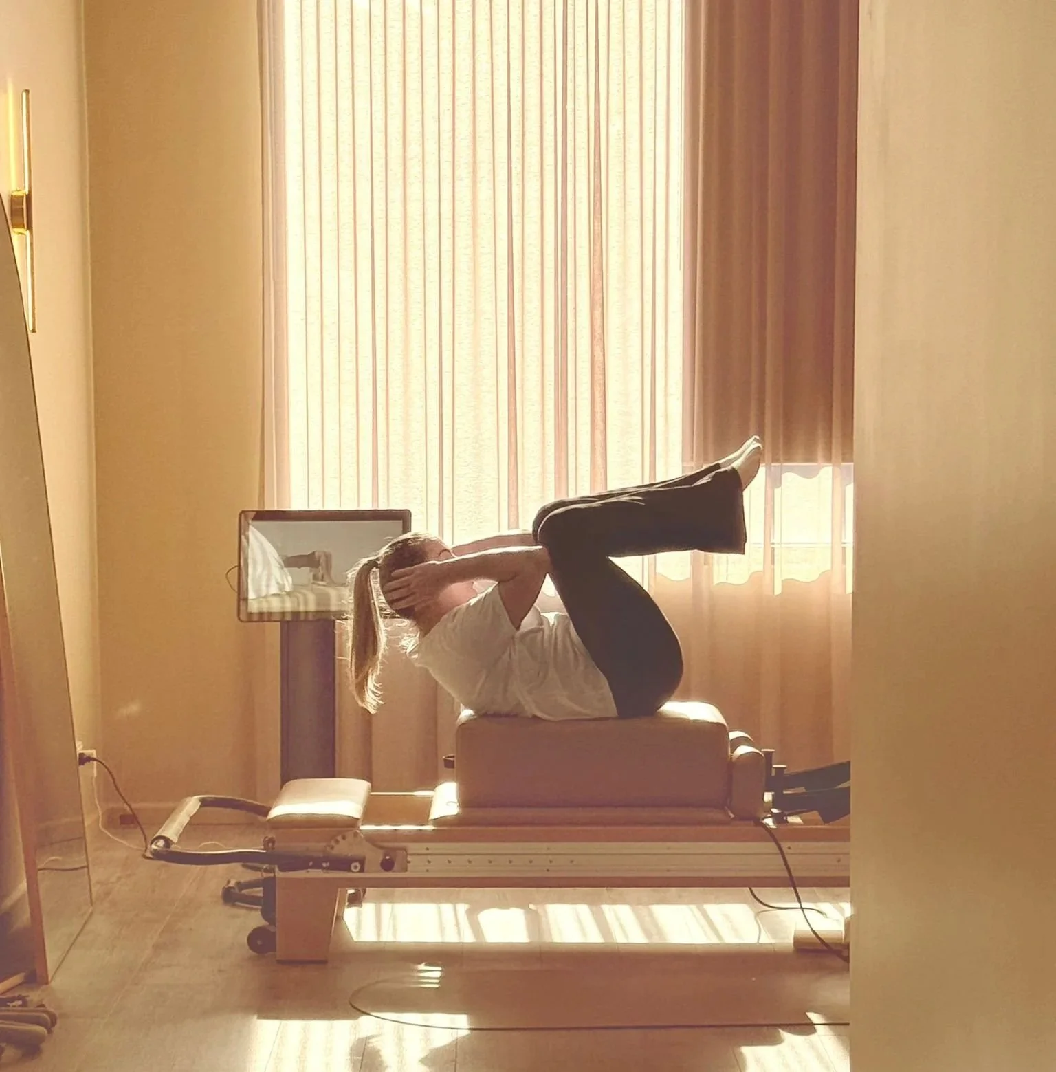 A person performing a yoga pose on a treatment table in a room with sunlight streaming through curtains.