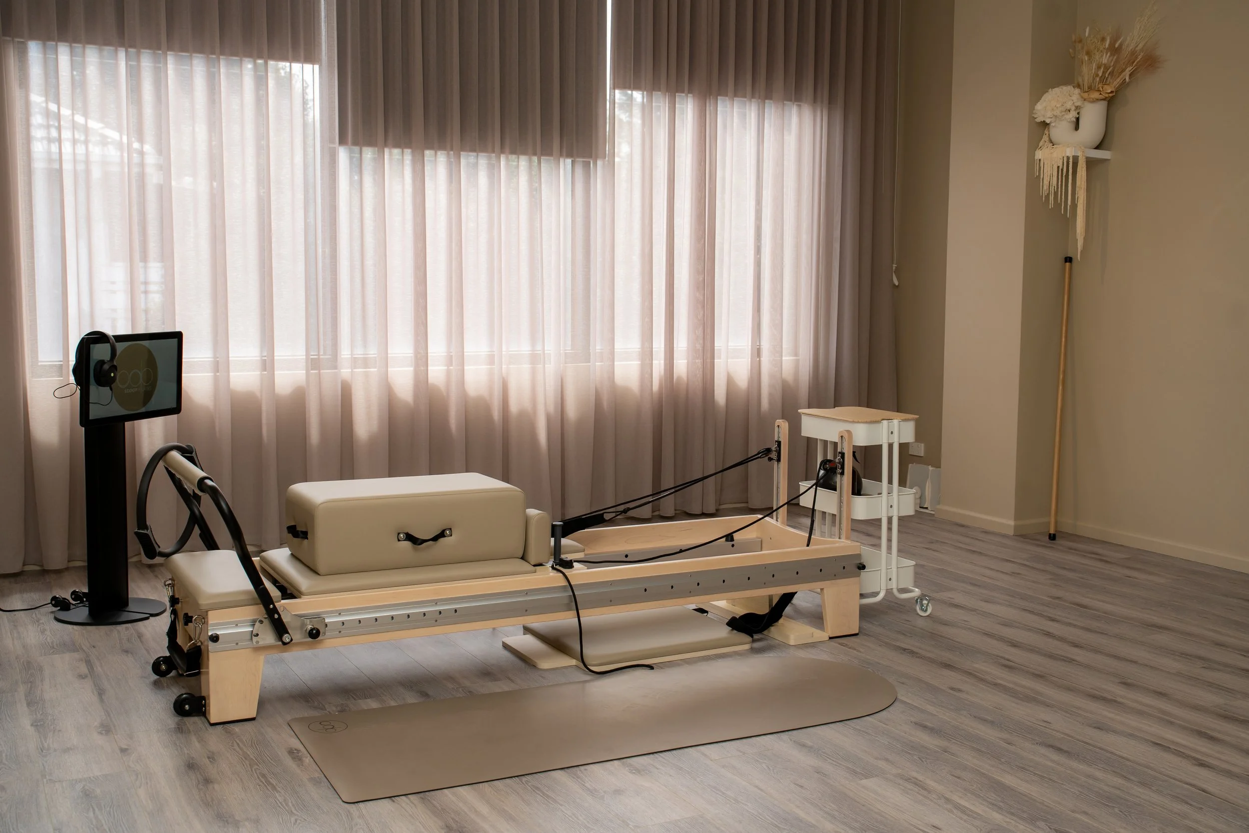 Hospital room with medical bed, wheelchair, and a monitor displaying a medical diagram, with sheer curtains covering large windows.