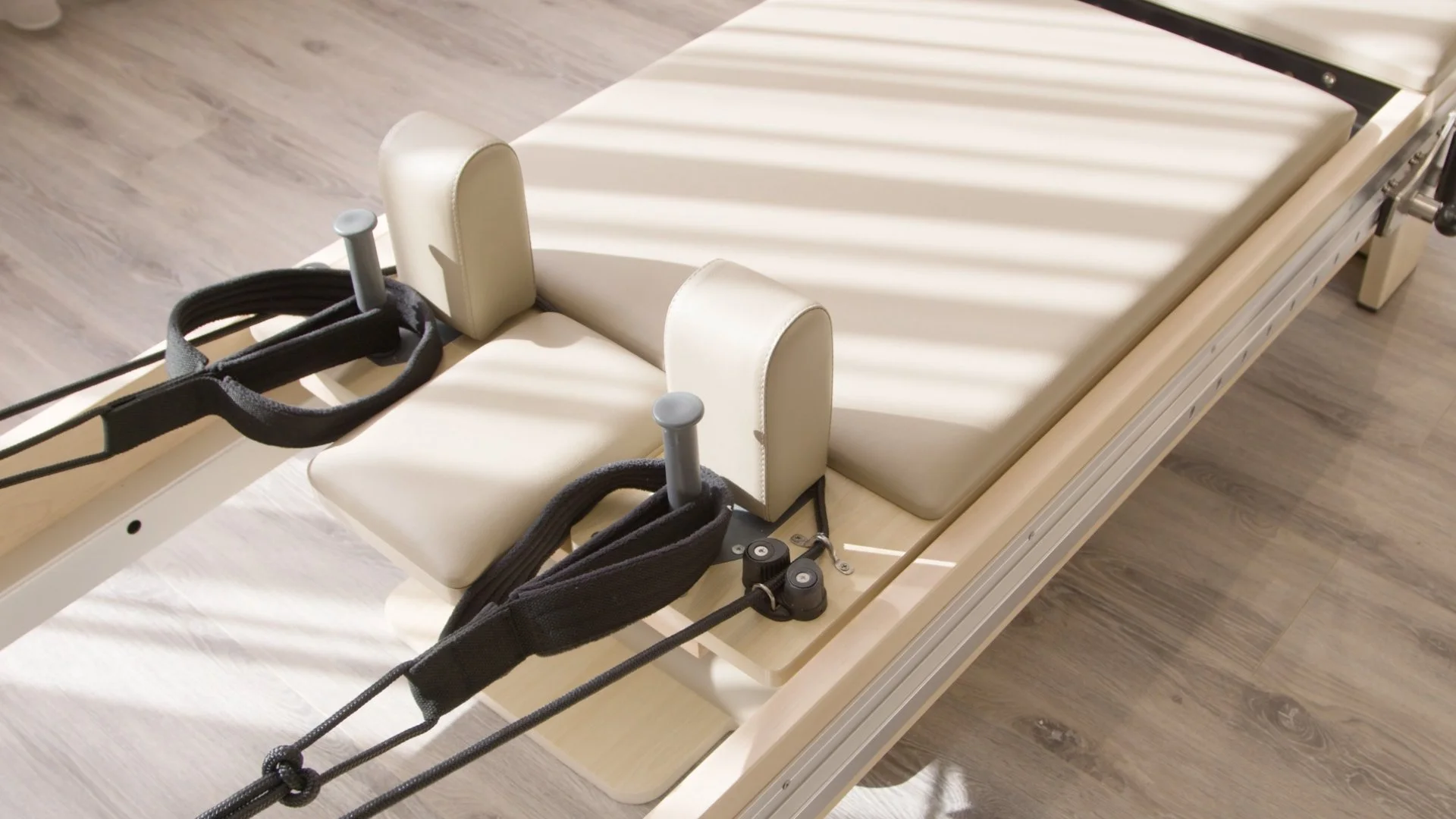 Hospital gurney with white padding, black straps, and beige side supports, set on a wooden floor.
